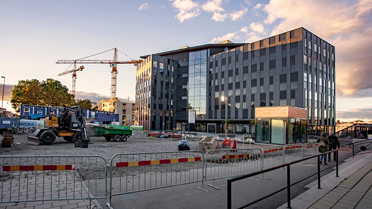 Modern kontorsbyggnad under konstruktion med kranar, barriärer och utrustning synliga.