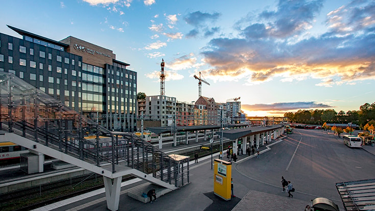 Modernt stadslandskap med byggkranar och en tågstation vid solnedgången.
