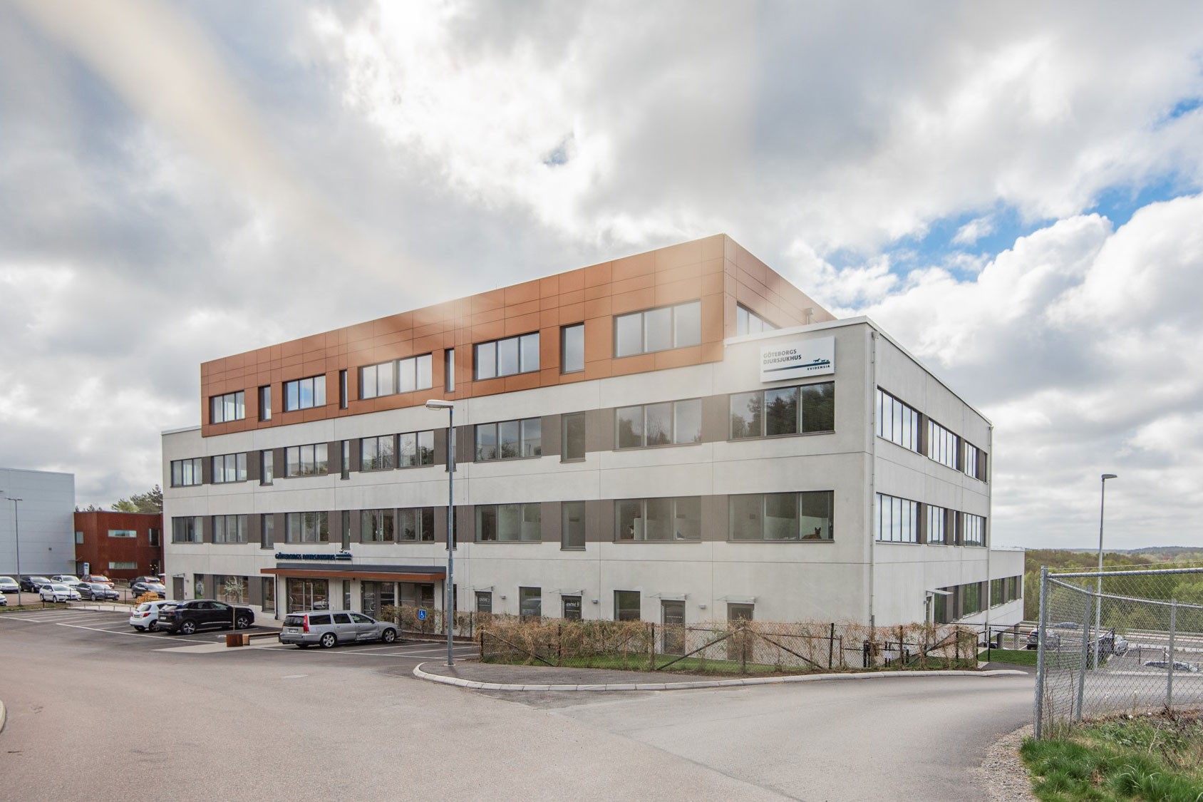 Modern fyravånings kontorsbyggnad med en blandning av vit och brun fasad under en molnig himmel.