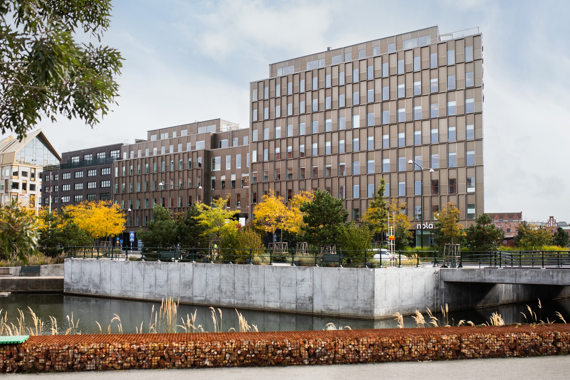 Moderna kontorsbyggnader med glasfönster vid en kanal och höstträd i förgrunden.