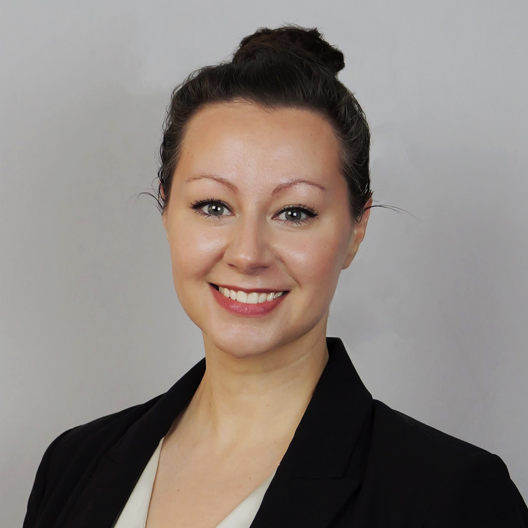 Professional woman in black blazer with hair in bun, neutral background Professional woman in black blazer with hair in a bun against a gray background.