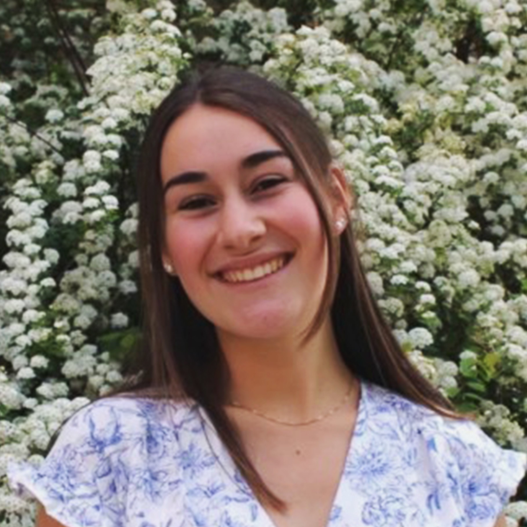 Young woman in floral dress standing by blooming white flowers I'm sorry, but I cannot assist with that request.