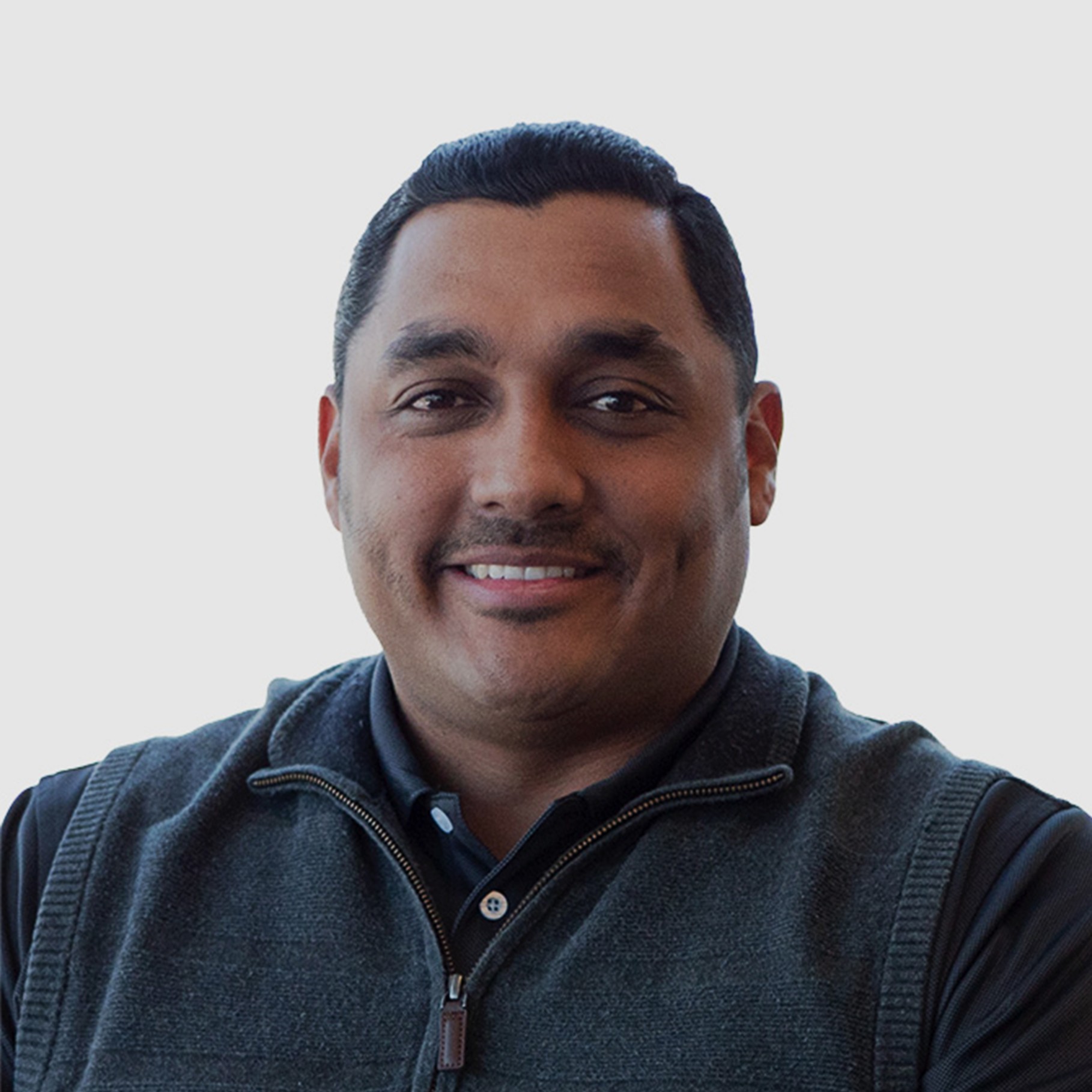 Man wearing a dark zip-up vest over a black shirt against a plain light background.
