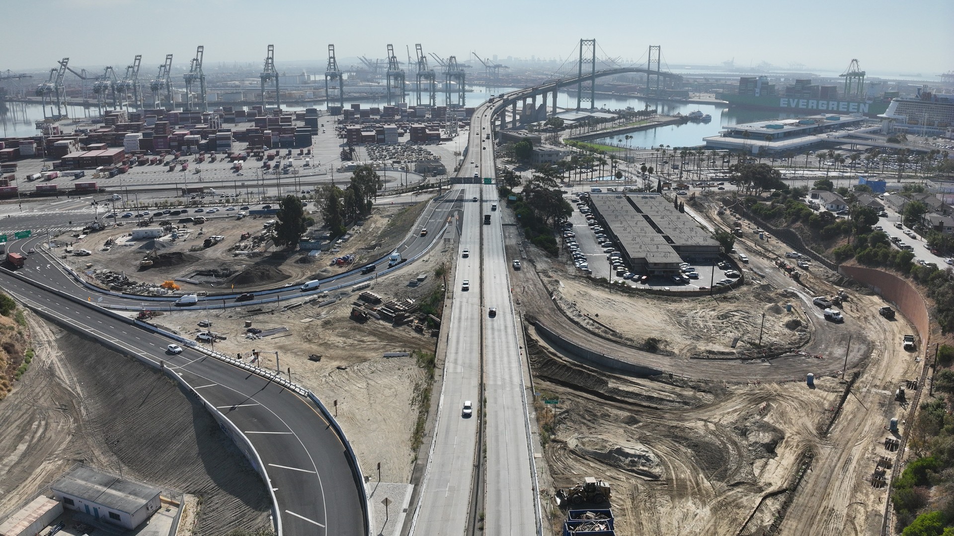 Aerial view of a busy port with container cranes, highway, and ongoing construction work.