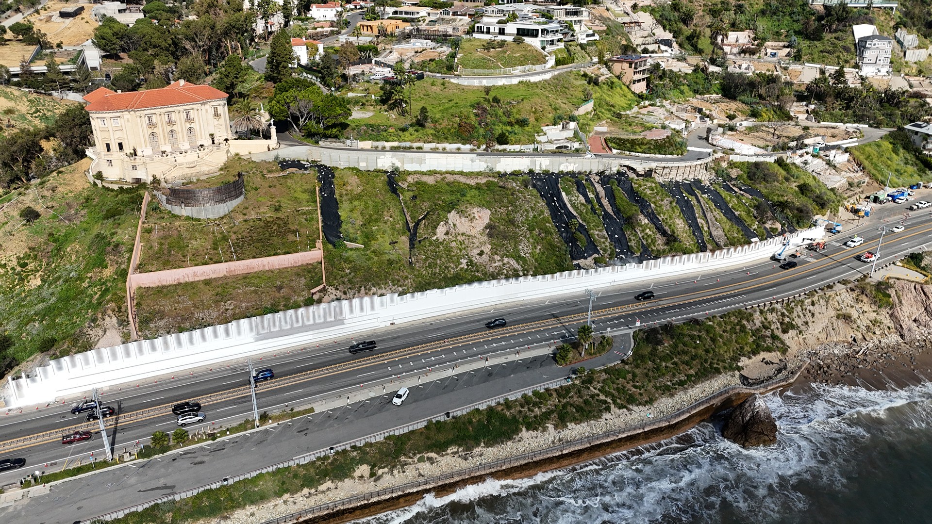 Getty Wall Emergency Restoration Along Pacific Coast Highway Coastal highway with cars beside cliffs and residential homes on a sunny day.