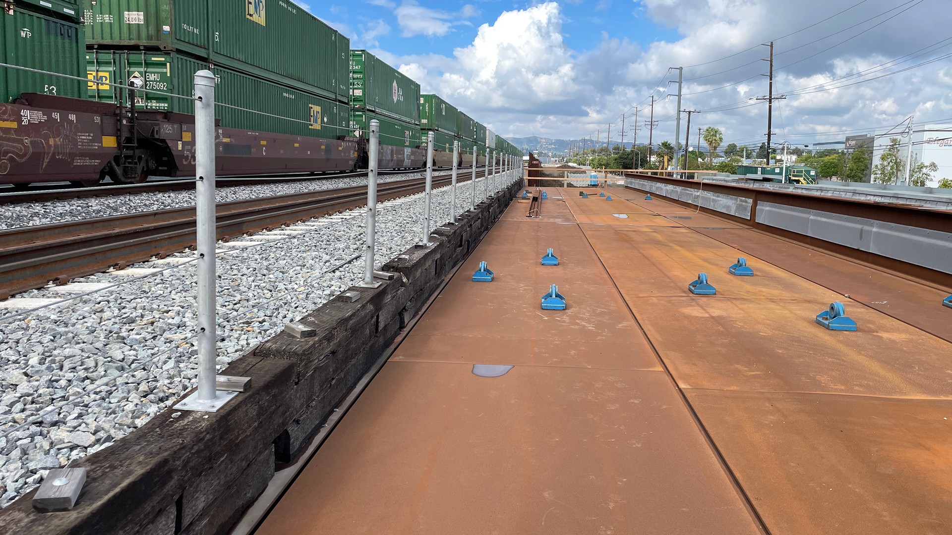 Railway tracks with stacked green cargo containers and rust-colored metal panels.