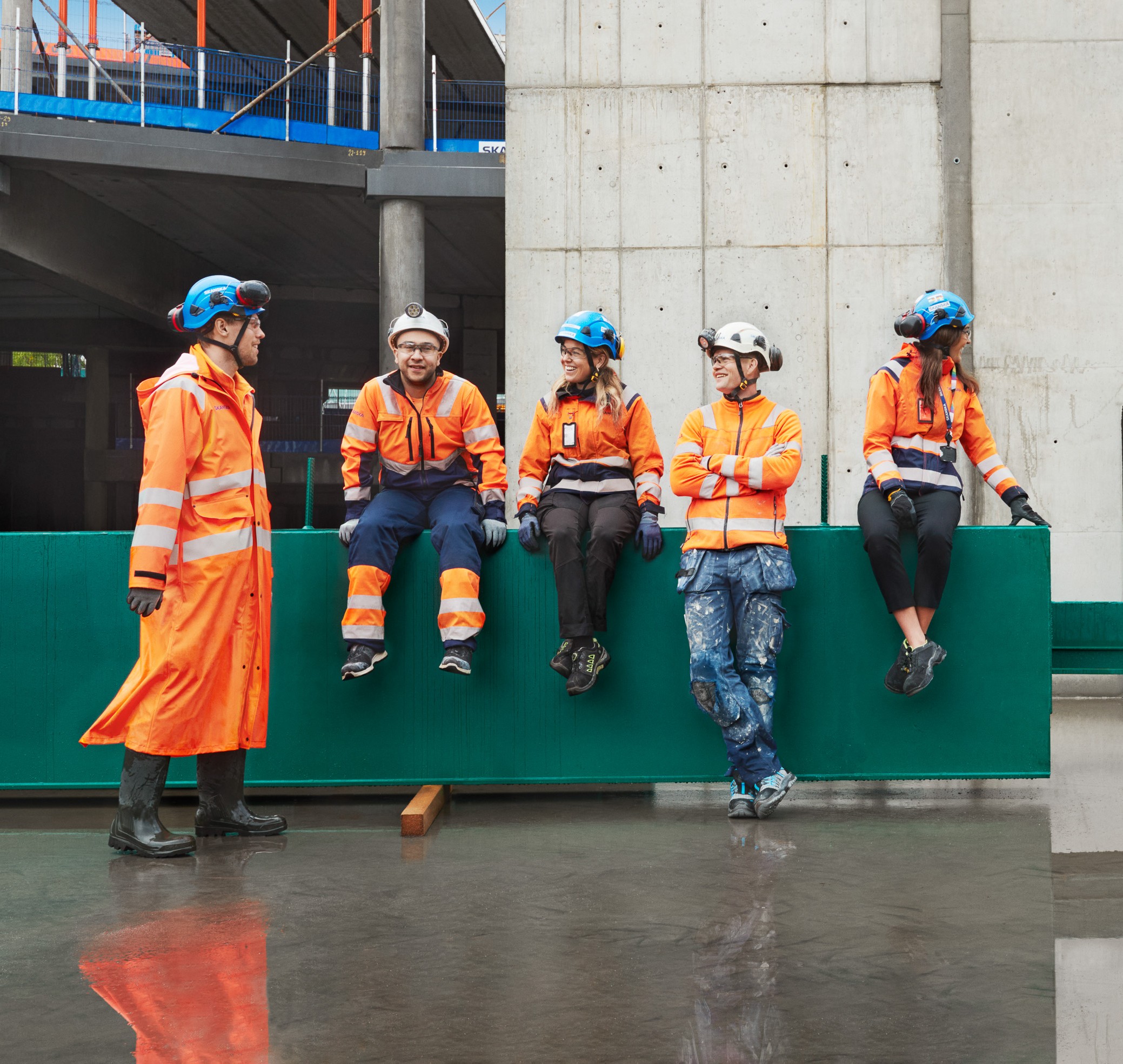 Construction workers in orange safety gear and helmets taking a break on site.