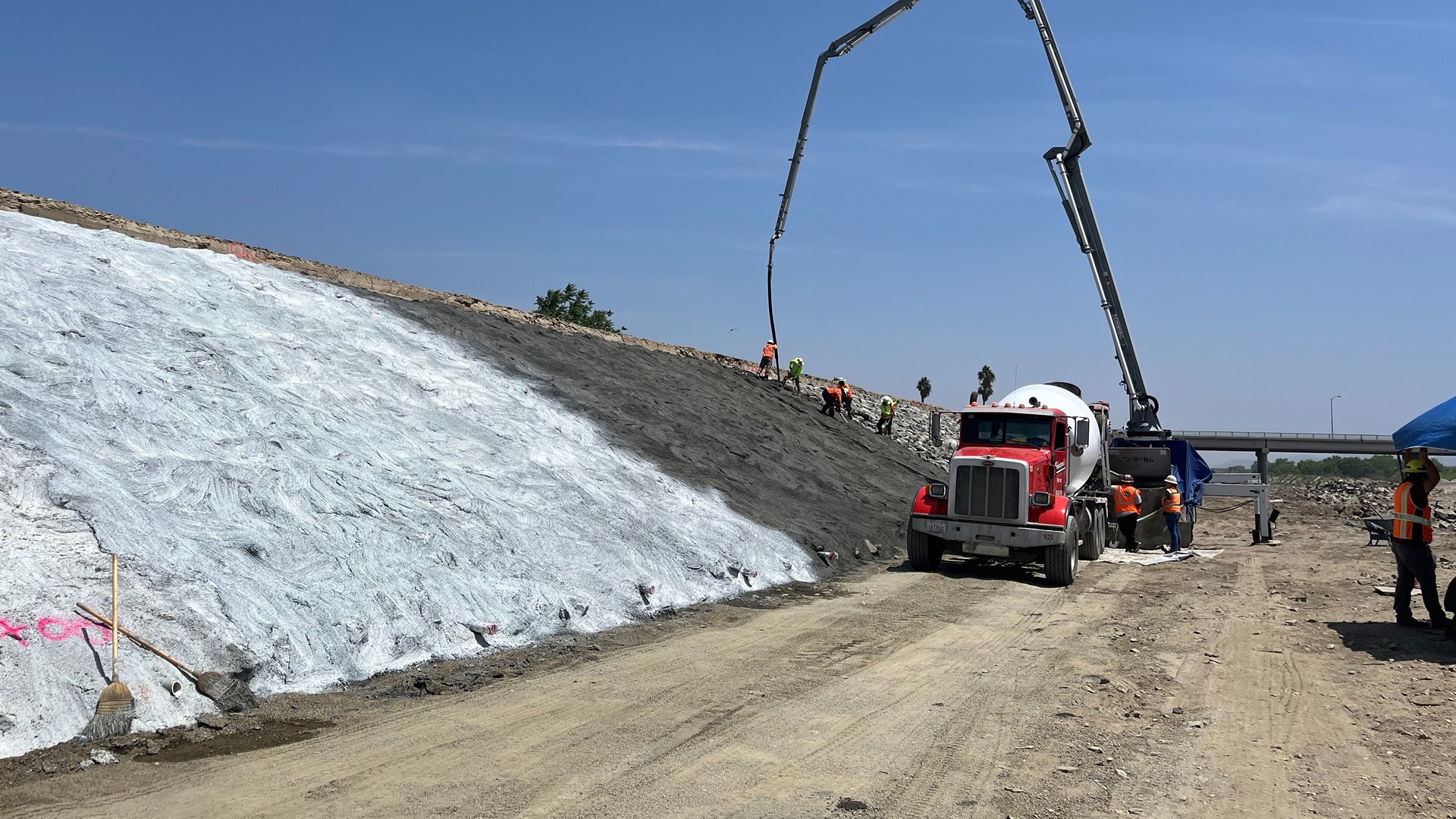 Construction workers use concrete pump truck to reinforce a large sloped embankment.