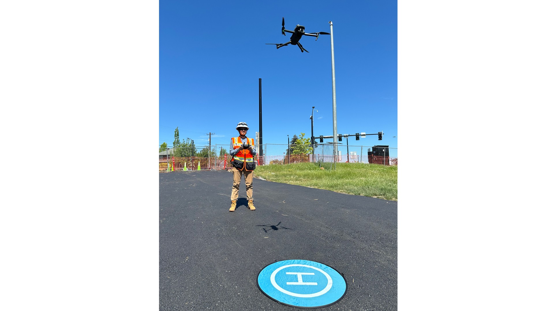 Person operating a drone near a landing pad on a clear sunny day outdoors.
