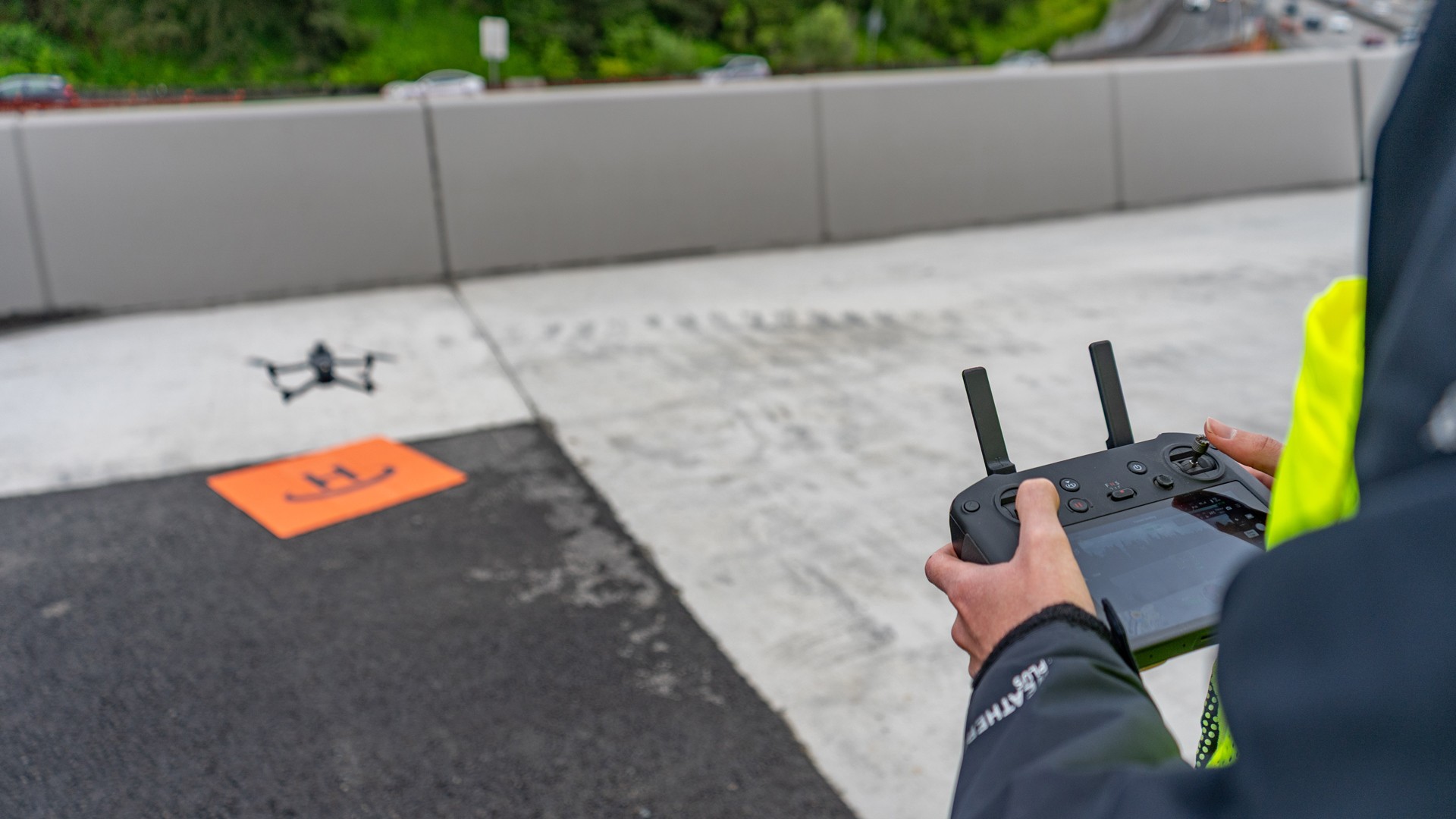 Person operating a drone with remote controller near an orange landing pad outdoors.