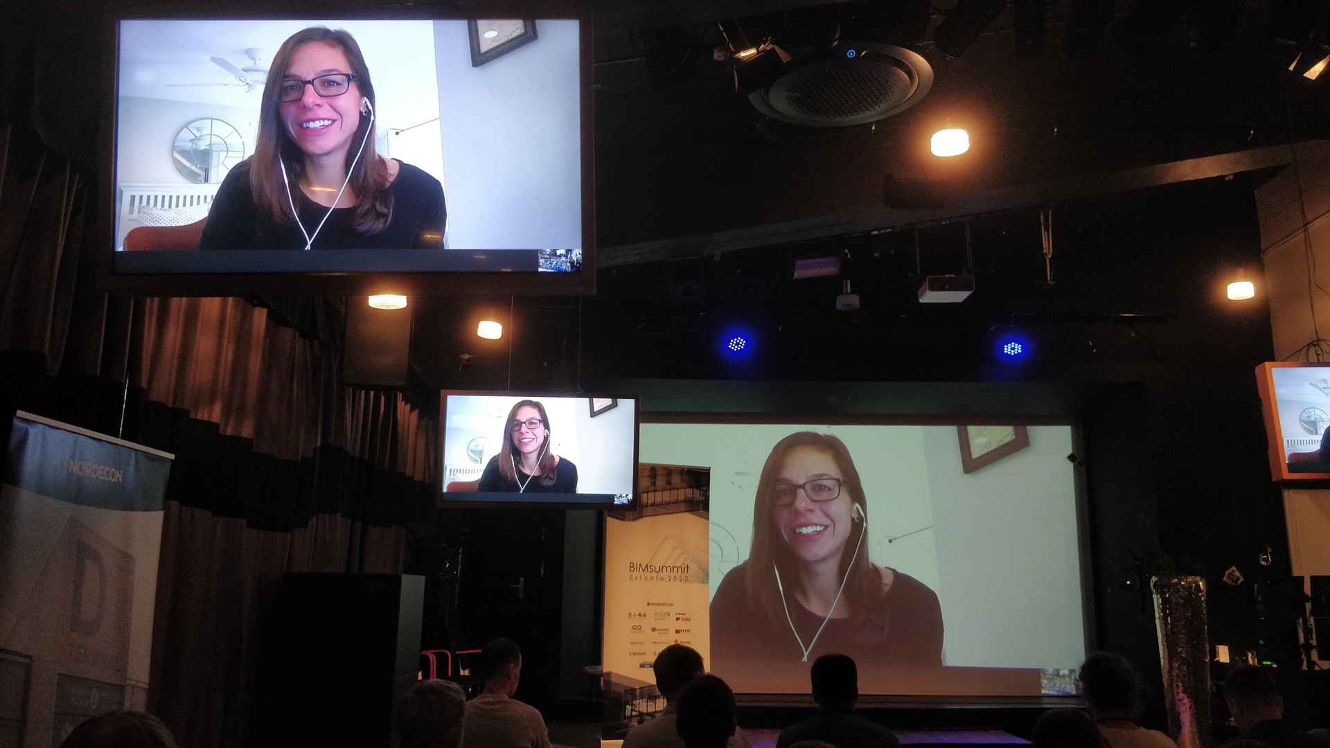 Virtual conference with multiple screens showing a remote speaker to an audience.