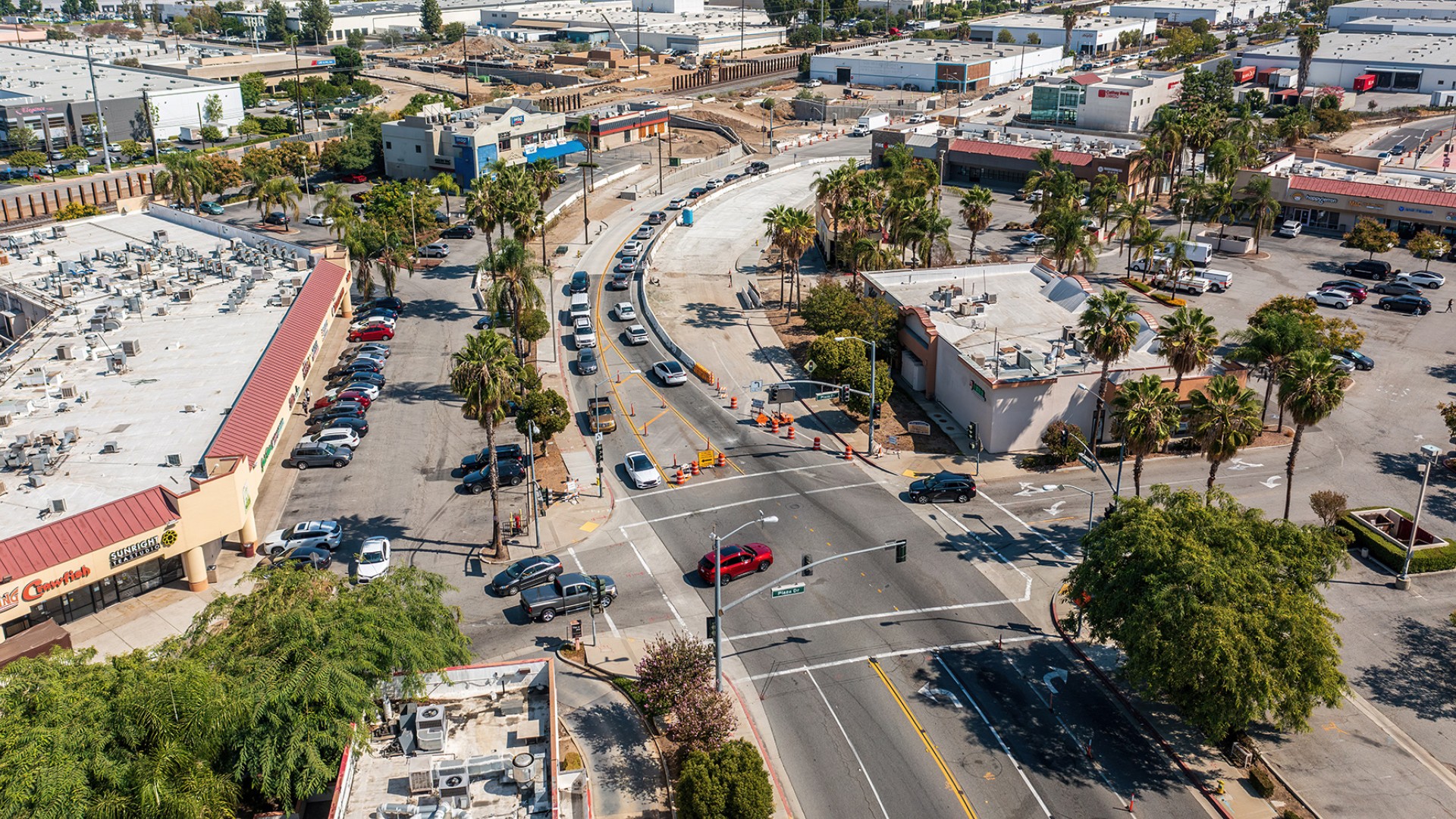 Aerial view of busy urban intersection with cars, palm trees, and commercial buildings.