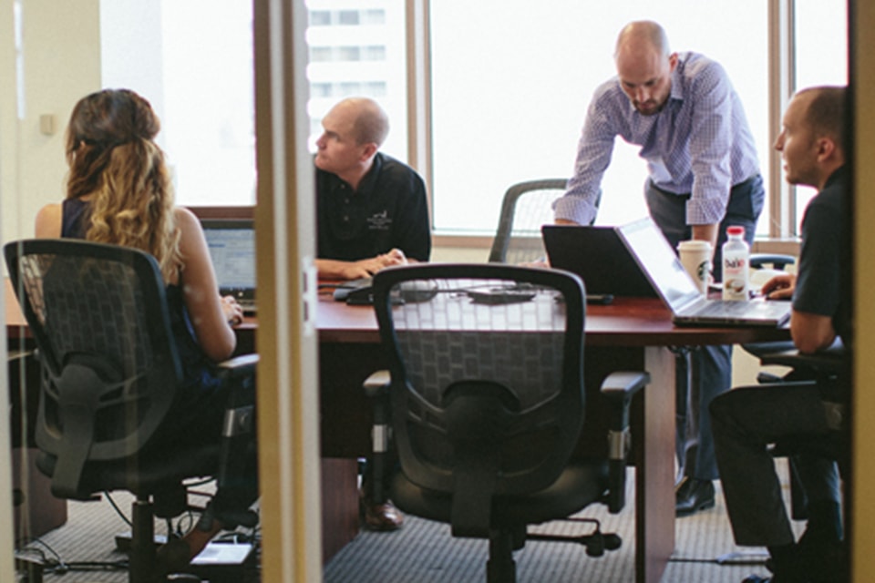 Four professionals in a modern office meeting, collaborating around a conference table.