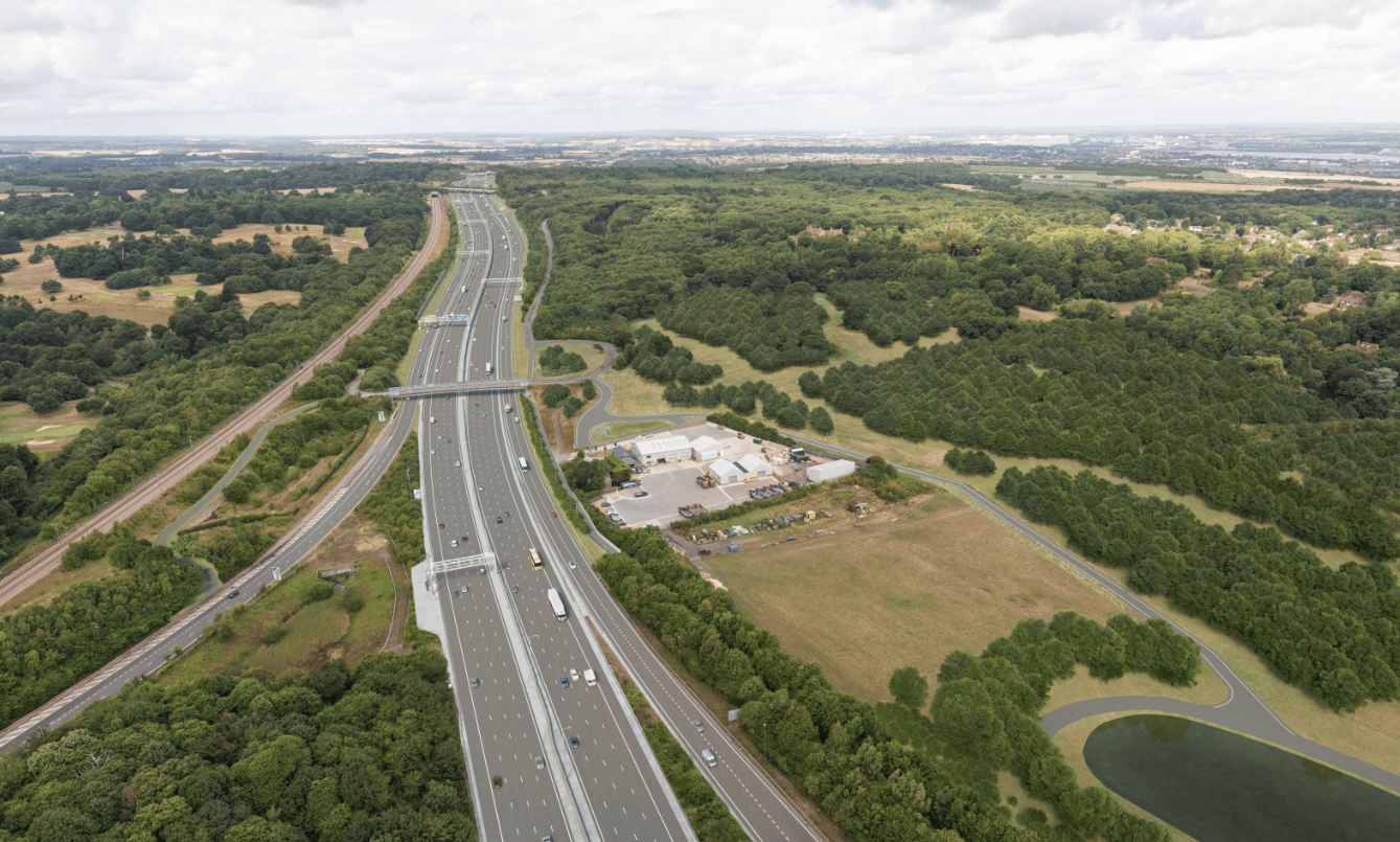 Aerial view of a busy highway surrounded by green trees and open fields under a cloudy sky.