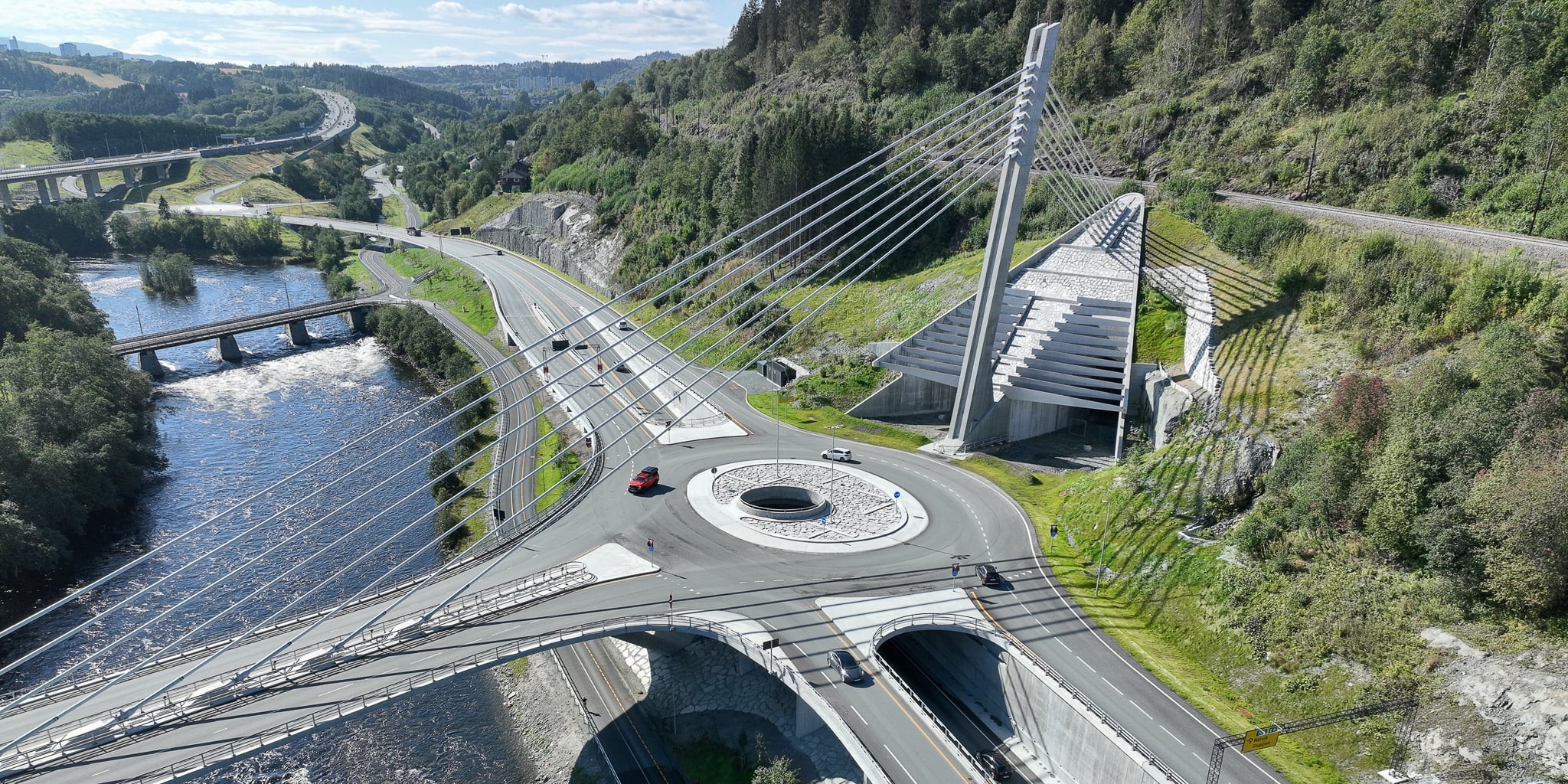 Aerial photo of a cable-stayed bridge with a unique circular roundabout over a scenic river landscape.