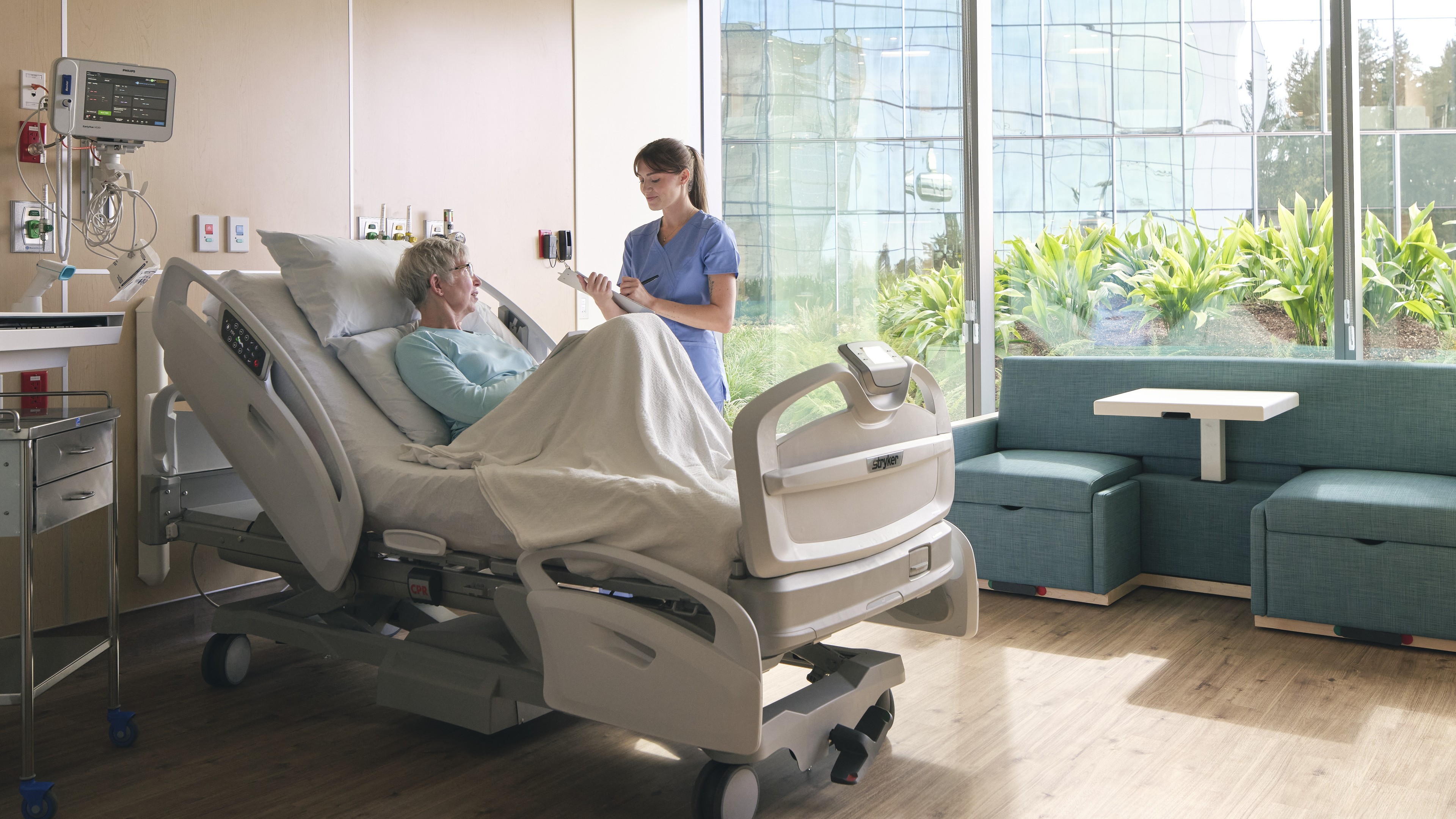 Nurse attending to a patient resting in a modern hospital room with natural light.