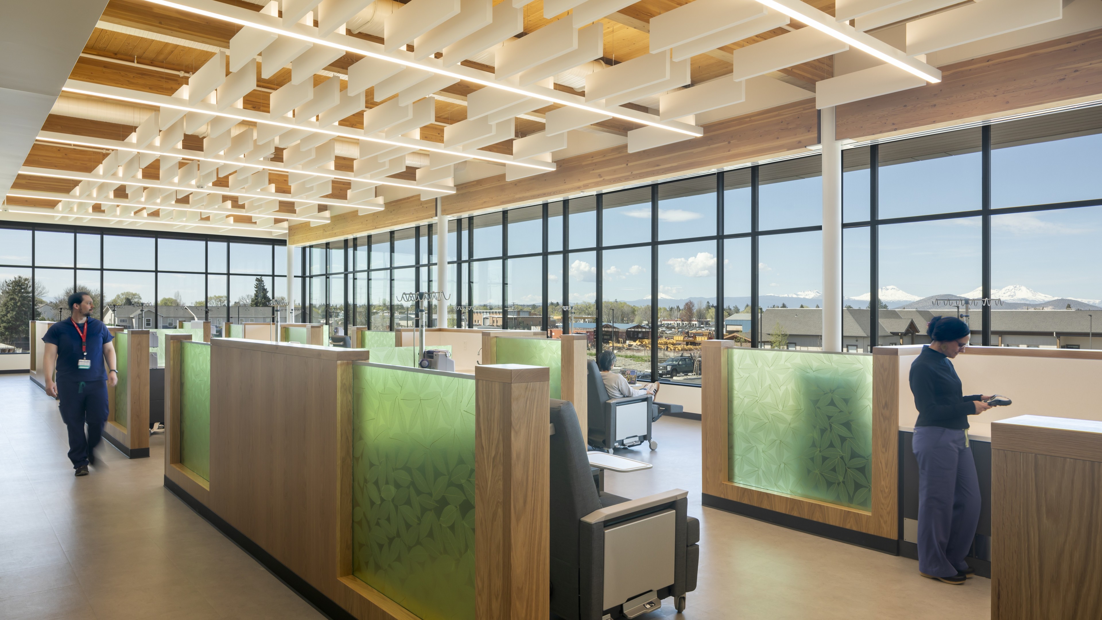 Modern office interior with wooden cubicles, large windows, and people working.