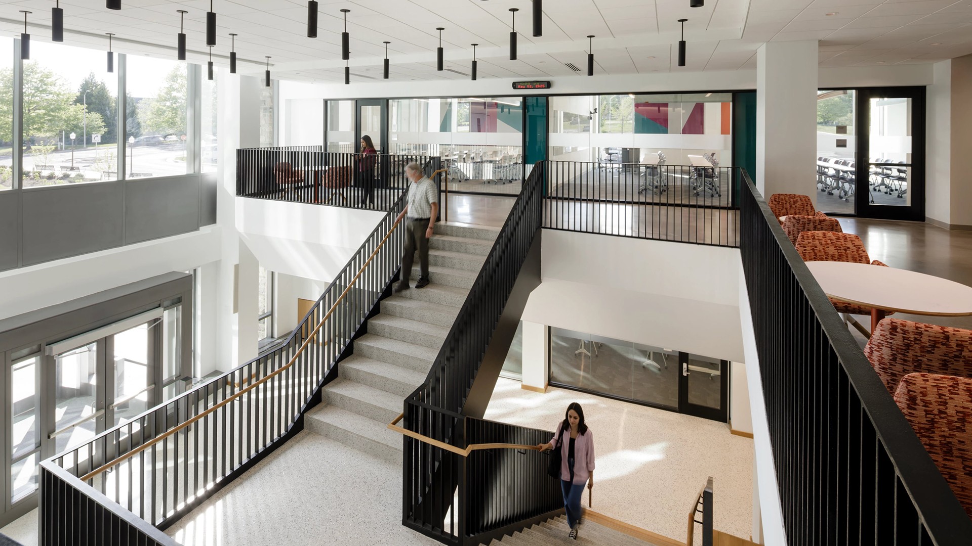 Modern office interior with stairs, glass walls, and people walking in a bright space.