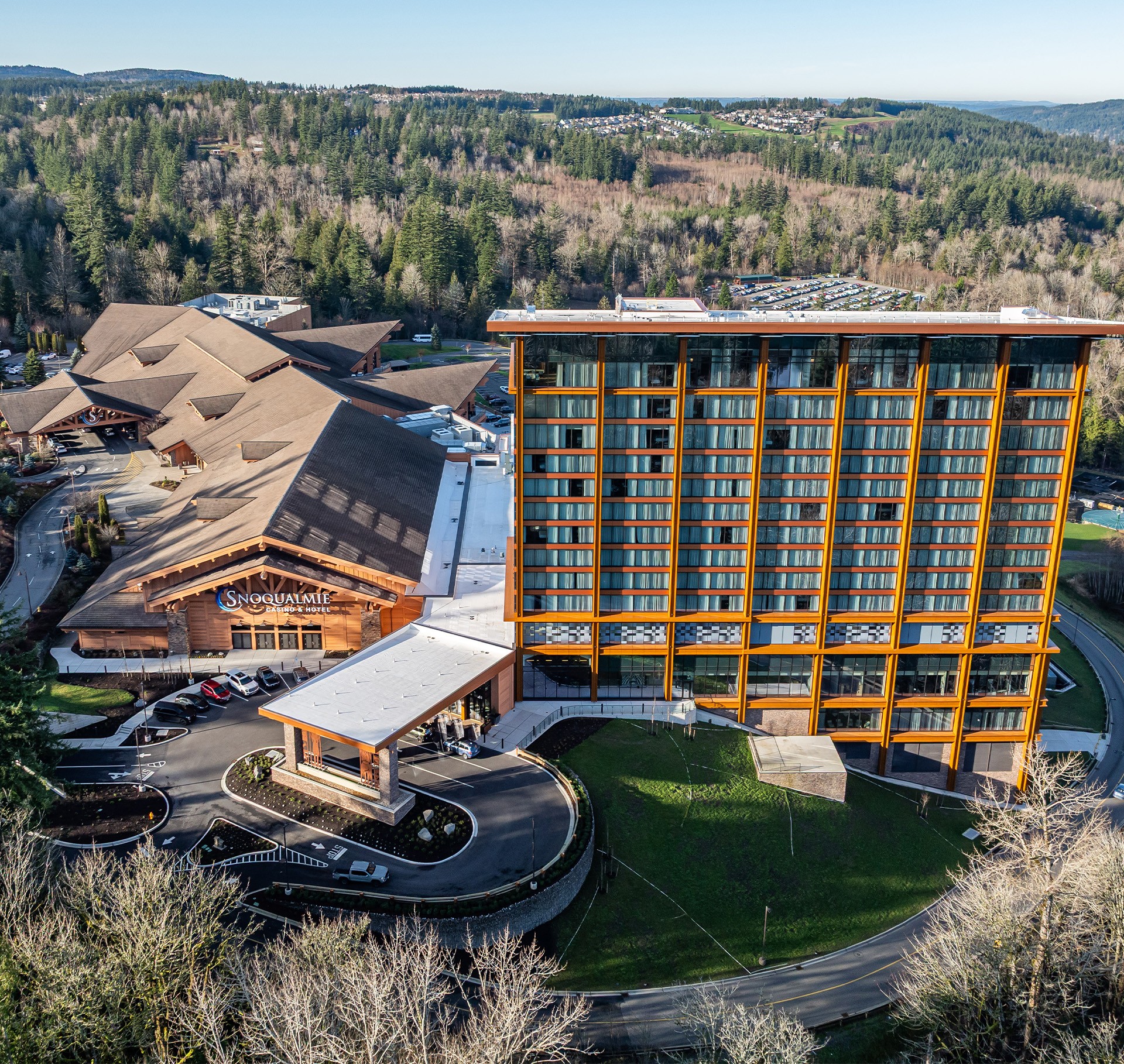 Aerial view of Snoqualmie Casino with surrounding forested hills under clear sky.