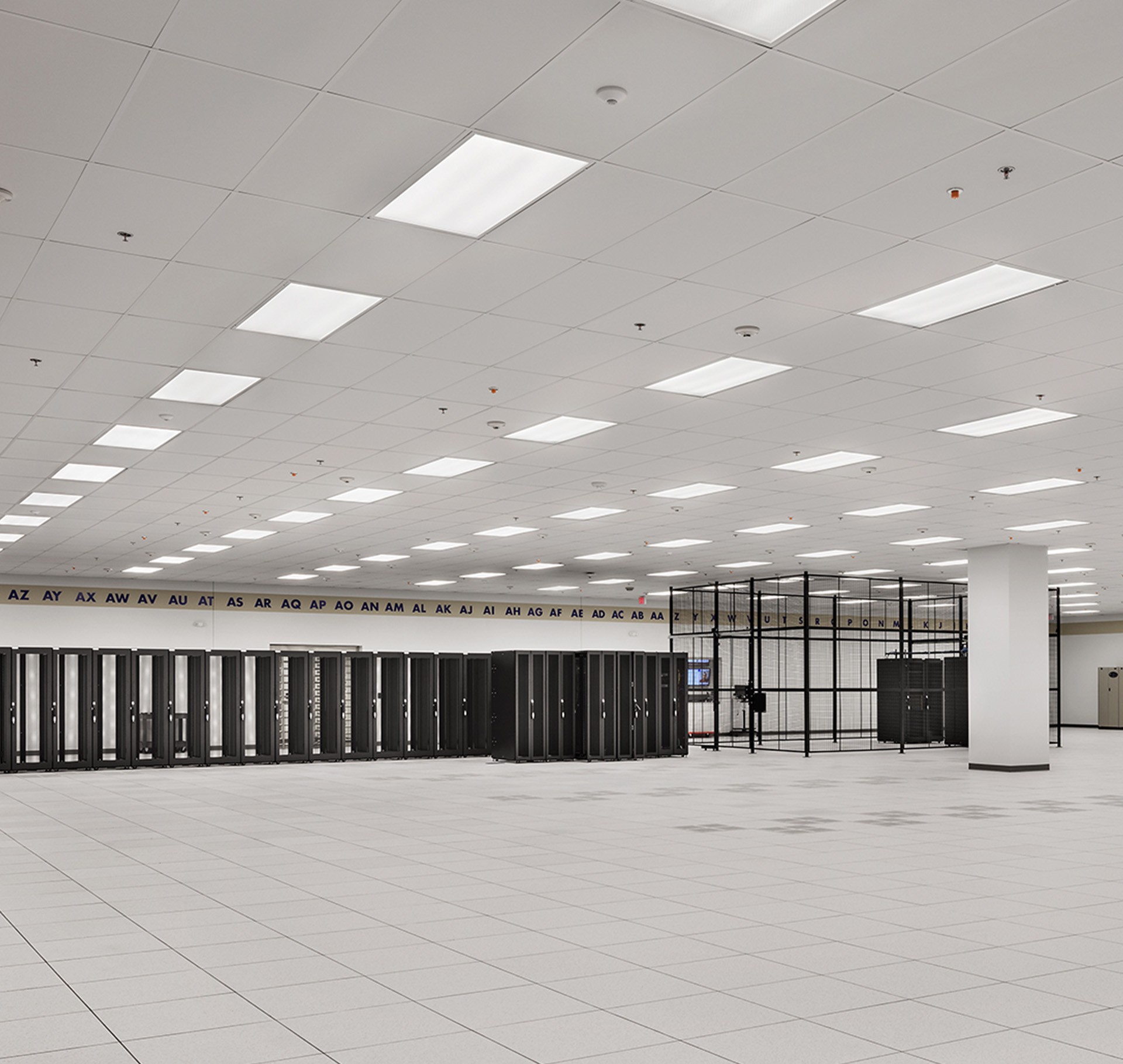 Modern Data Center Server Room with Advanced Equipment Rows Spacious, modern data center with rows of black server racks and bright ceiling lights.