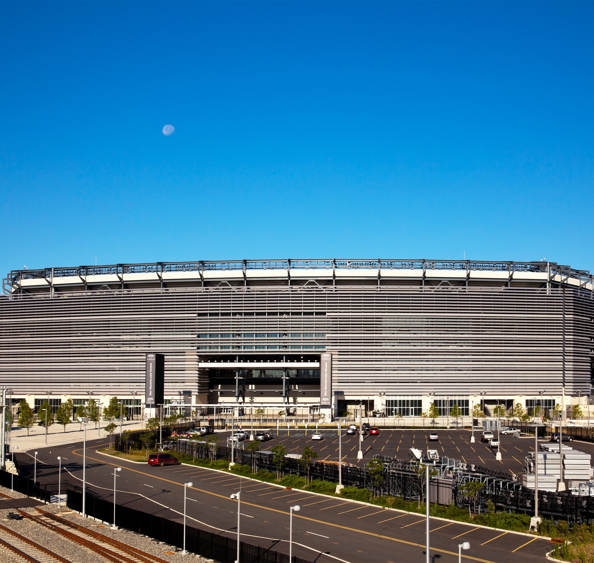 Large modern stadium with striped facade and empty parking lot under clear blue sky with moon.