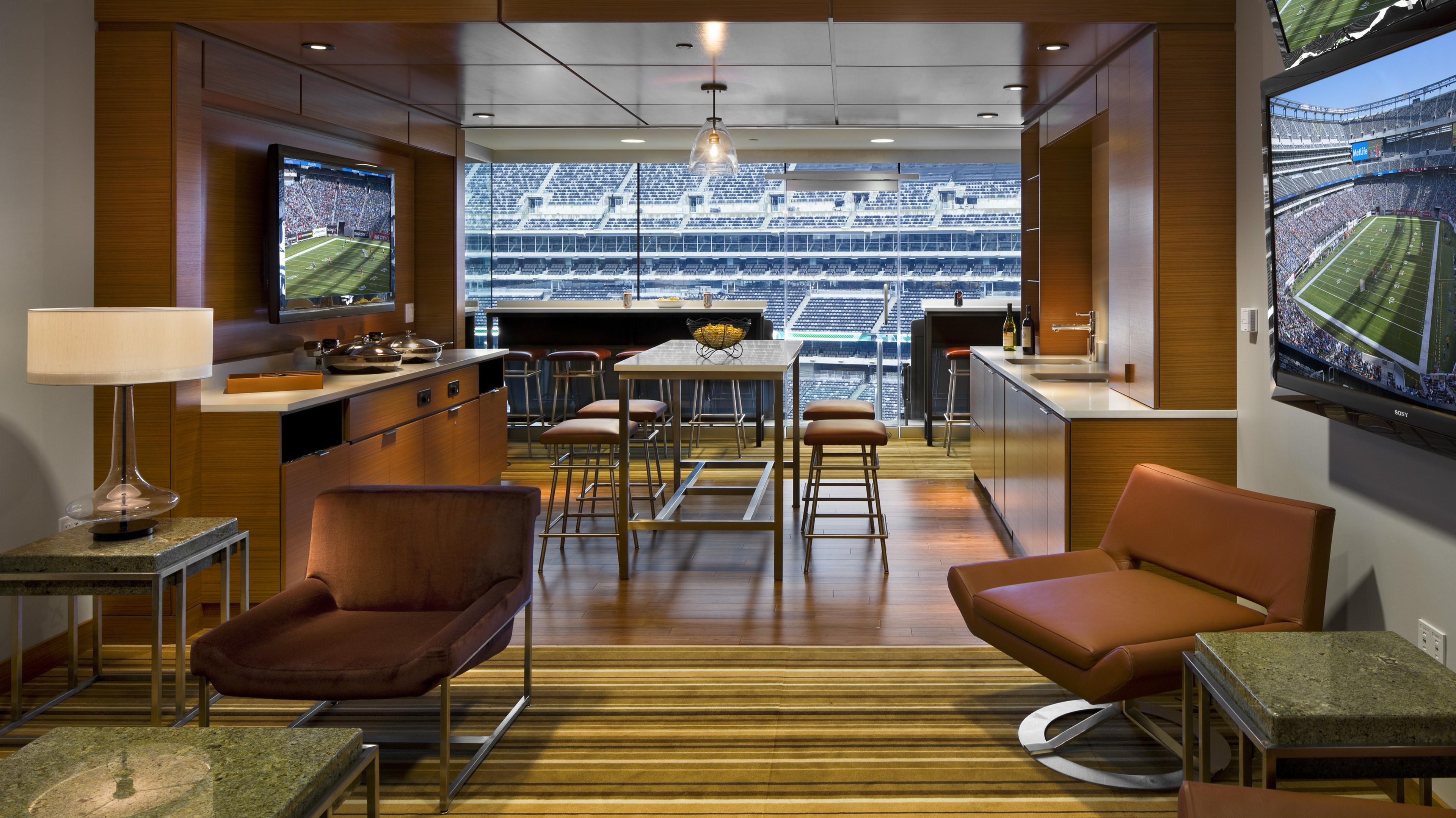 Luxury stadium suite with modern seating, large windows, and sports game on TVs.