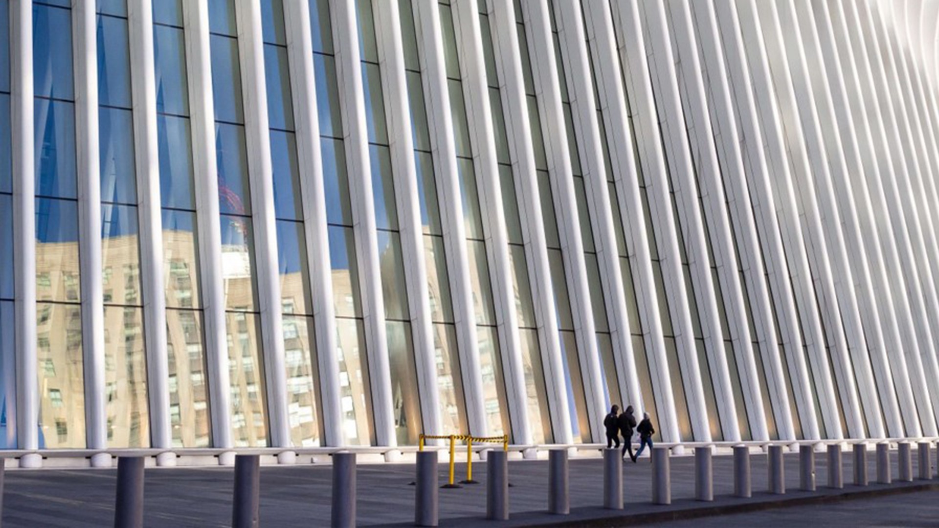 Modern architectural structure with tall vertical beams and people walking nearby.