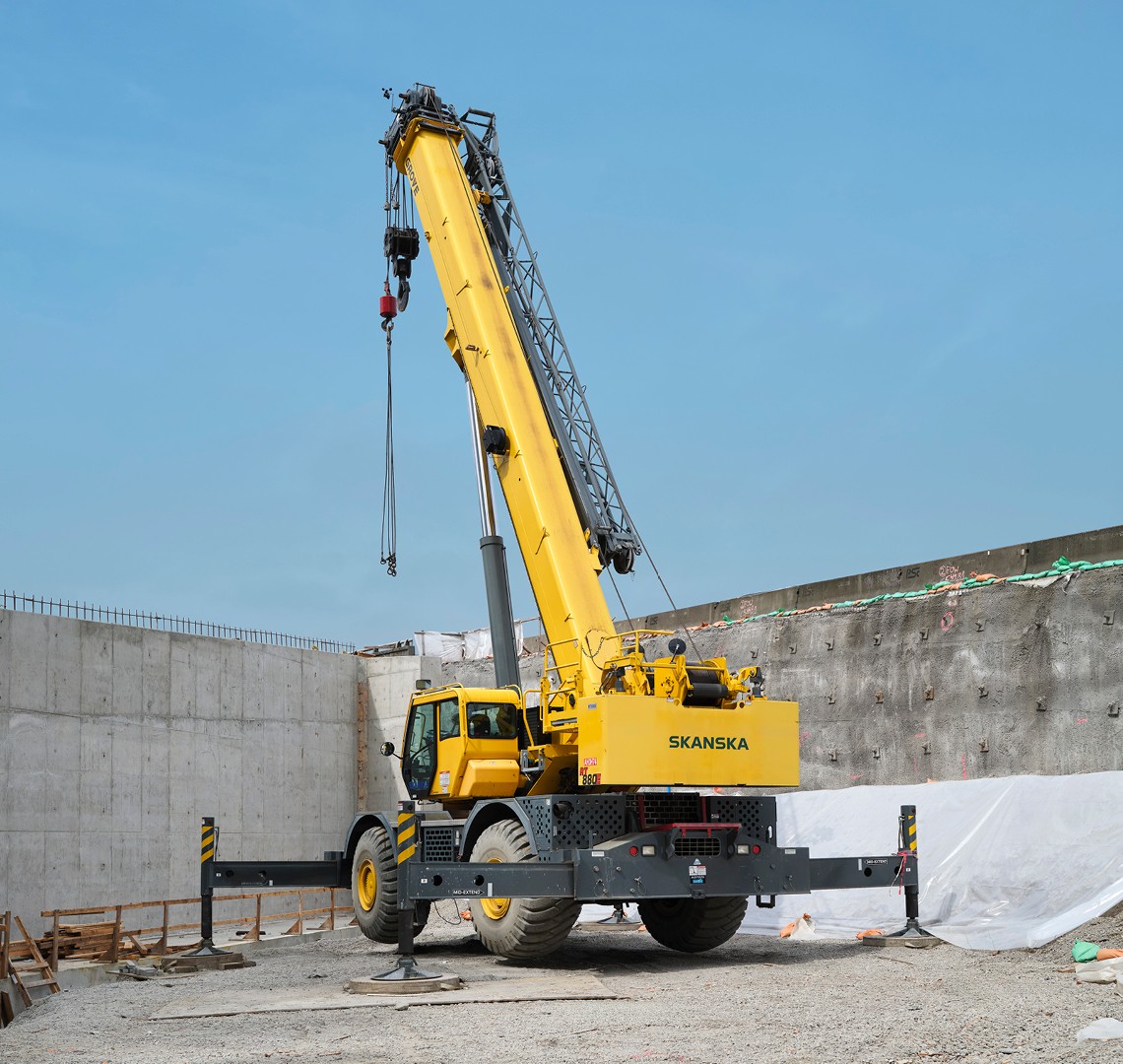 Yellow mobile crane with extended boom operating at a construction site with concrete walls.