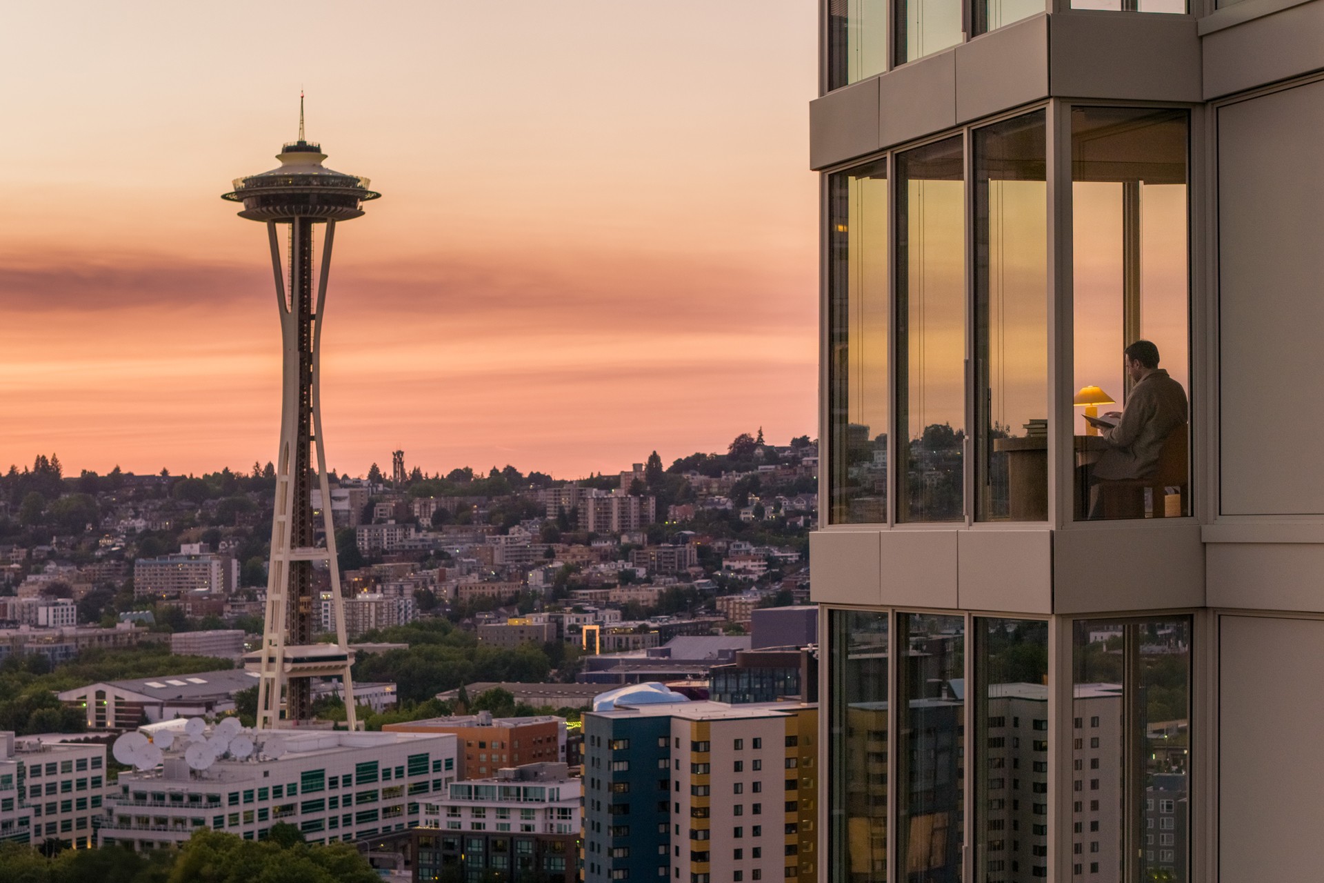 Seattle skyline at sunset with Space Needle and office view Man working in a high-rise office with Seattle Space Needle and cityscape at sunset.