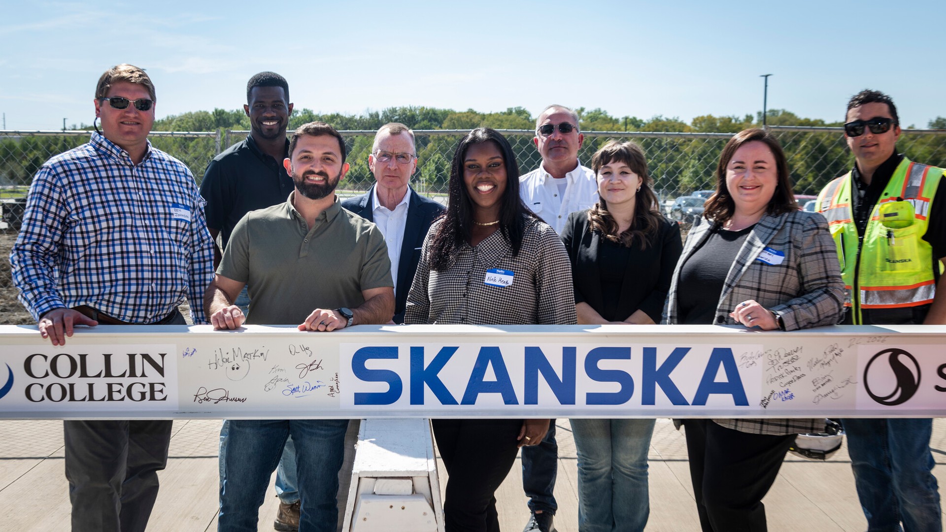Group of diverse professionals holding a signed Skanska ribbon at a Collin College event.
