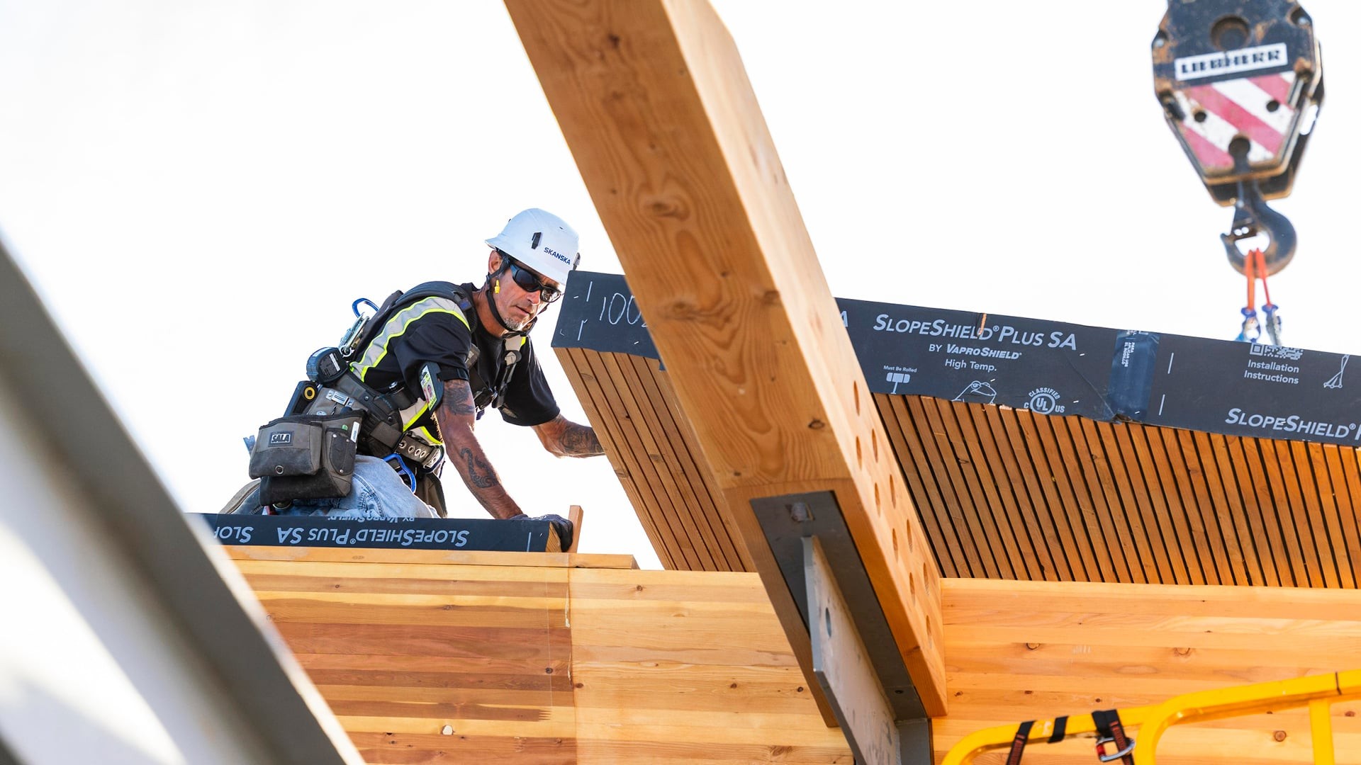 Construction worker wearing safety gear installs wooden beams on building site.