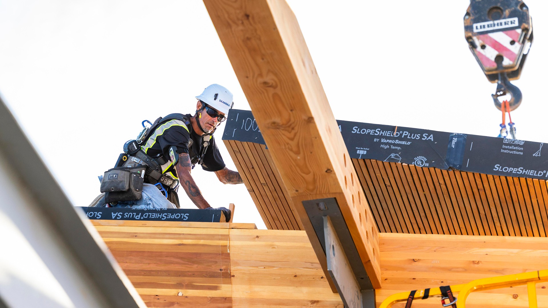 Mass Timber Beam Lift at Active Airport Construction Site Construction worker wearing safety gear installs wooden beams on building site.