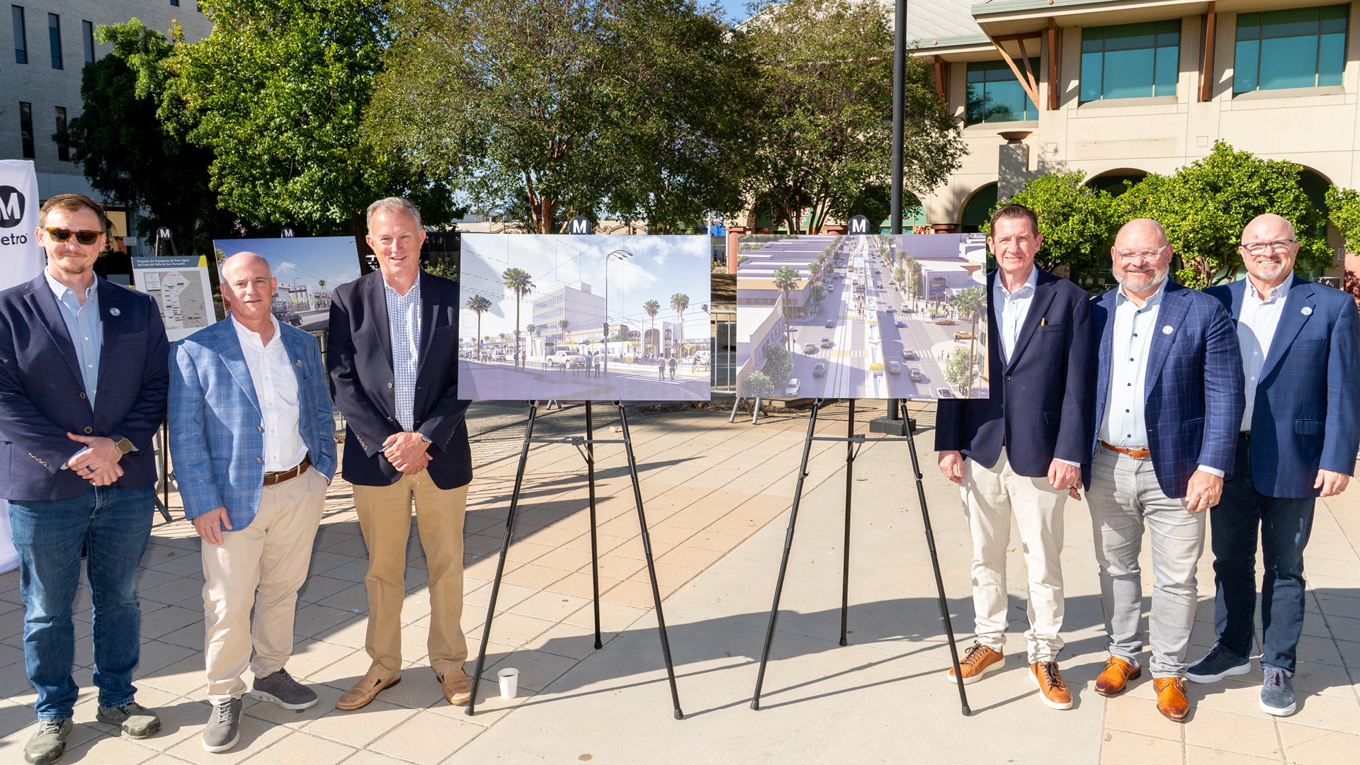 East San Fernando Valley Light Rail Transit Project Groundbreaking Six men in business casual attire stand outdoors beside display boards with urban development plans.