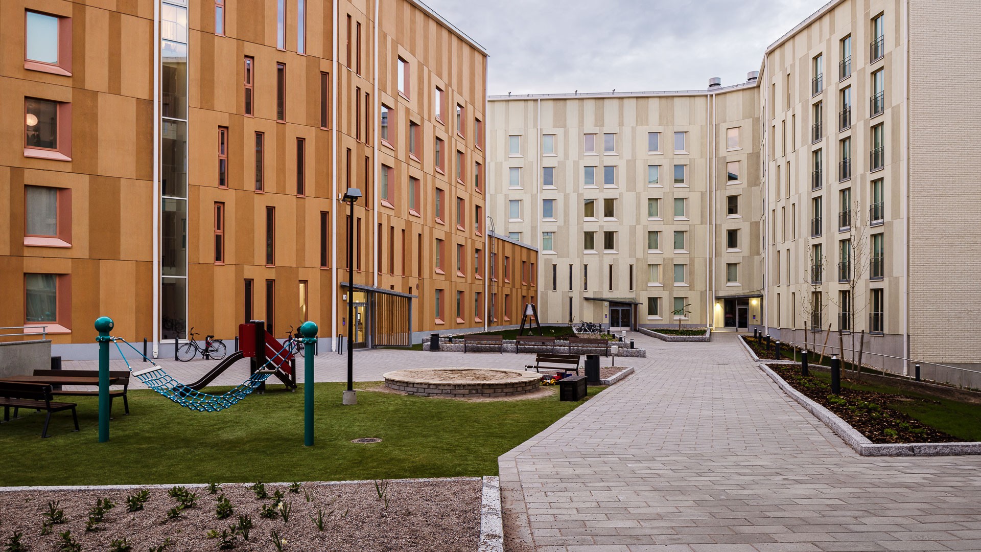 Viihtyisällä yhteispihalla on myös lapsille leikkipaikka. Moderni asuinkerrostalo leikkipaikalla ja istutetulla polulla kaupunkialueella.