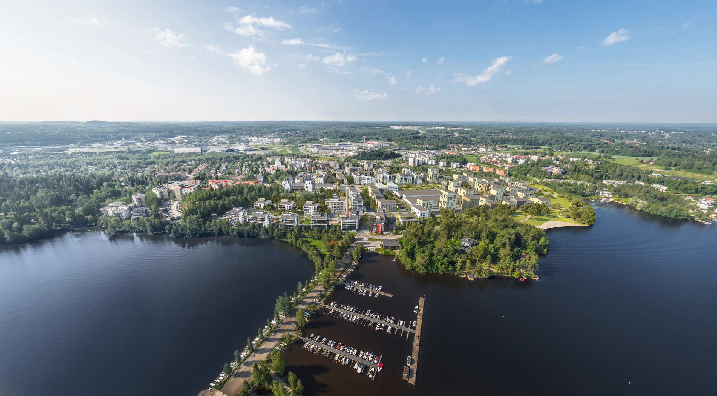 Härmälänranta Ilmakuva viehättävästä järvenrantakaupungin maisemasta, jossa on rehevää kasvillisuutta ja venesatama kirkkaan taivaan alla.