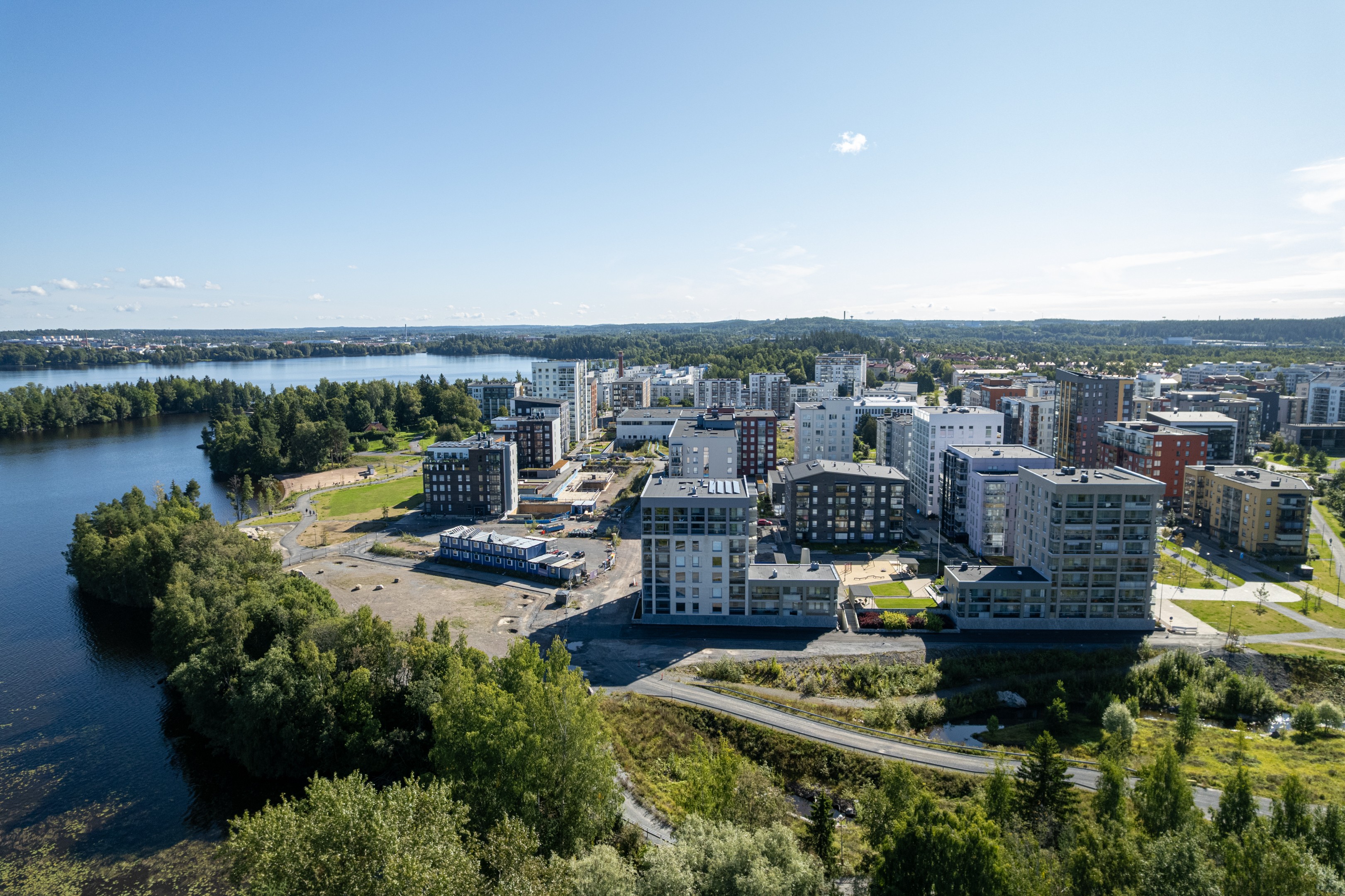 Kerrostaloja vihreiden puistoalueiden ympäröimänä, jotka sijaitsevat järven rannalla.