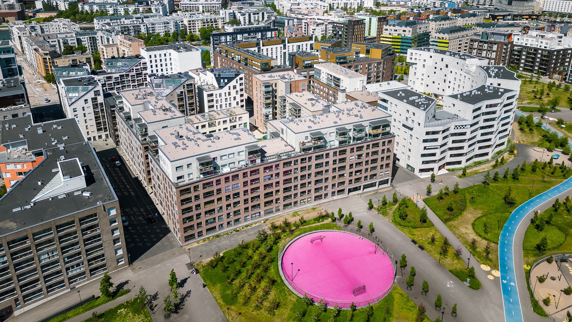 Ilmakuva nykyaikaisista kaupunkirakennuksista, joissa on elinvoimainen pinkki pyöreä koripallokenttä ja vihreitä alueita.