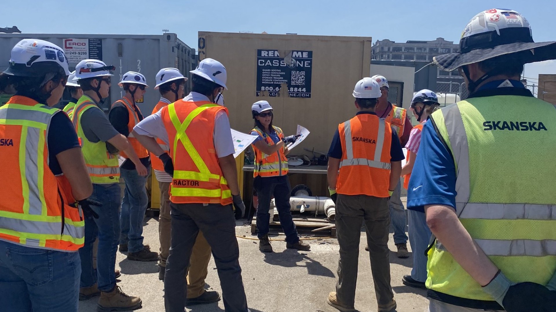 Construction workers wearing safety gear and helmets gathered for a site briefing.