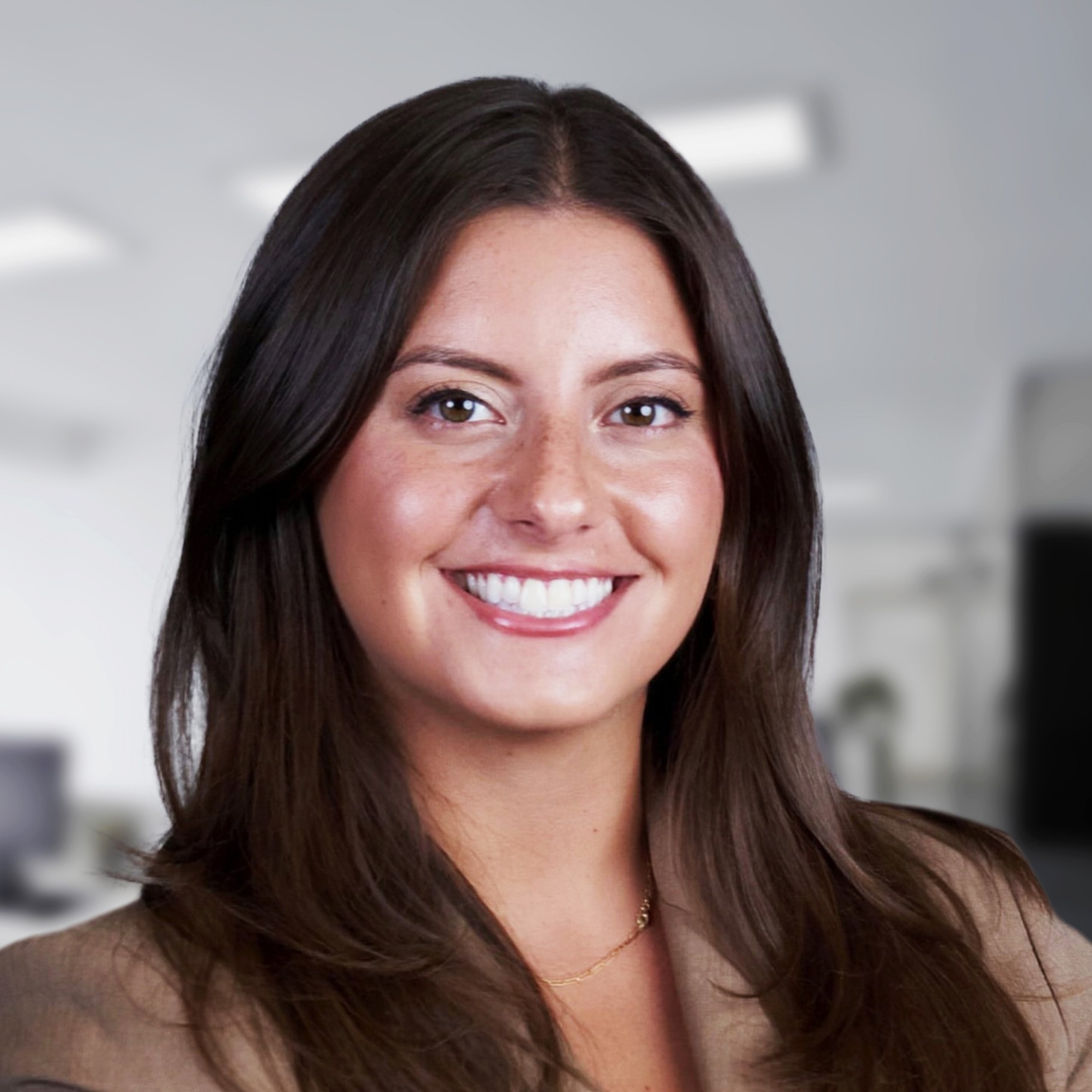 Professional woman with long dark hair wearing a brown blazer in an office setting.