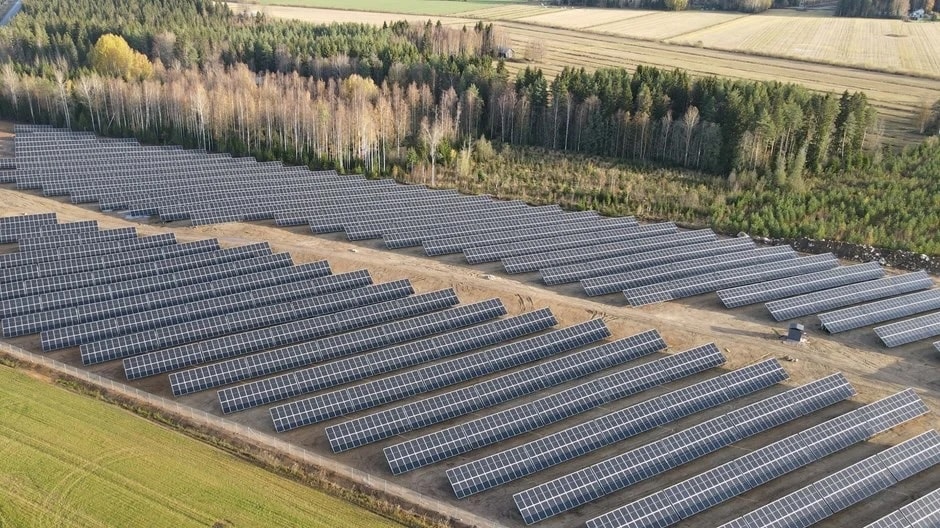 Flygfoto av en stor solpanelsanläggning omgiven av träd och åkrar.