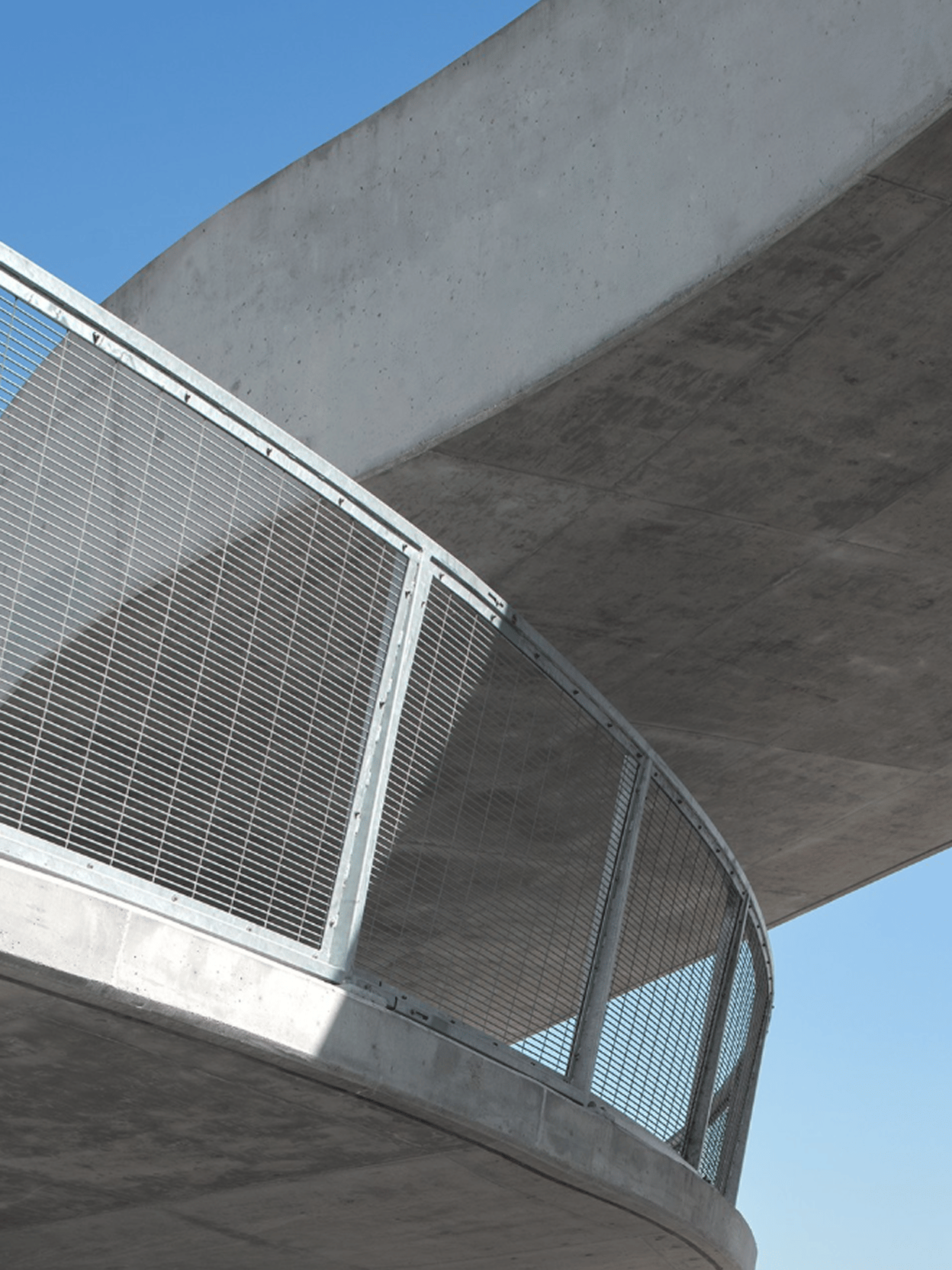 Modern concrete walkway with metal railing curves under blue sky.