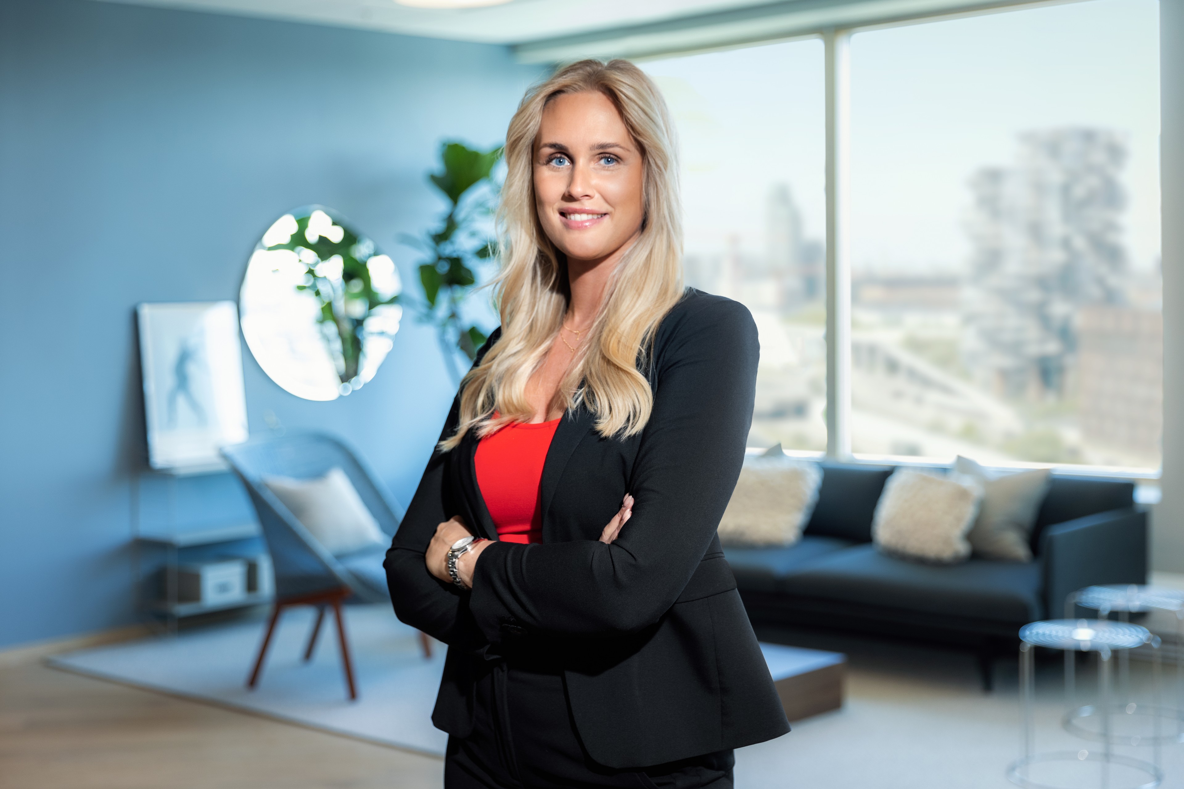 Professionel kvinde i en sort blazer og rød top, der står i et moderne kontor.