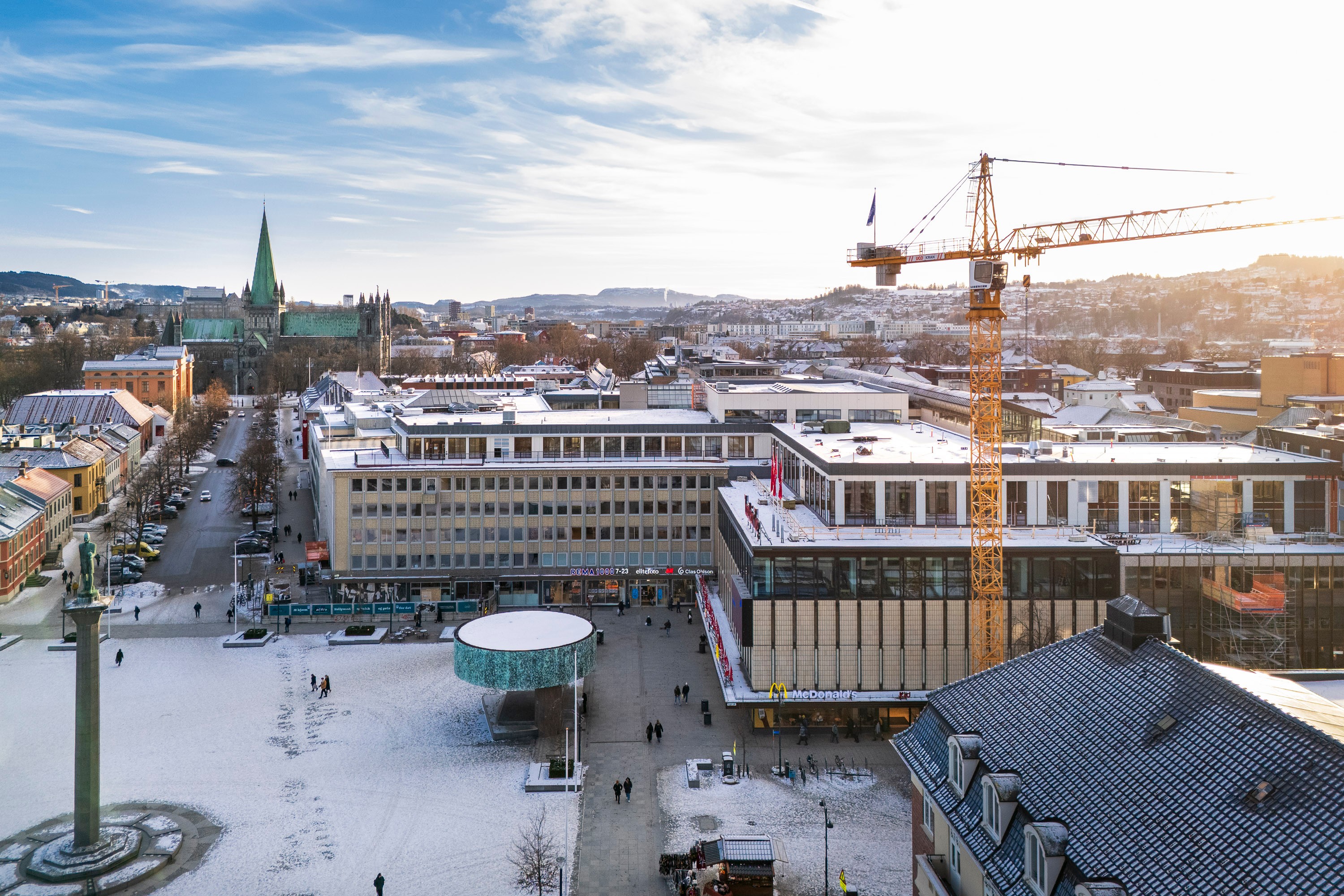 Bybilde med en byggekran, snødekte gater og historiske bygninger om vinteren.