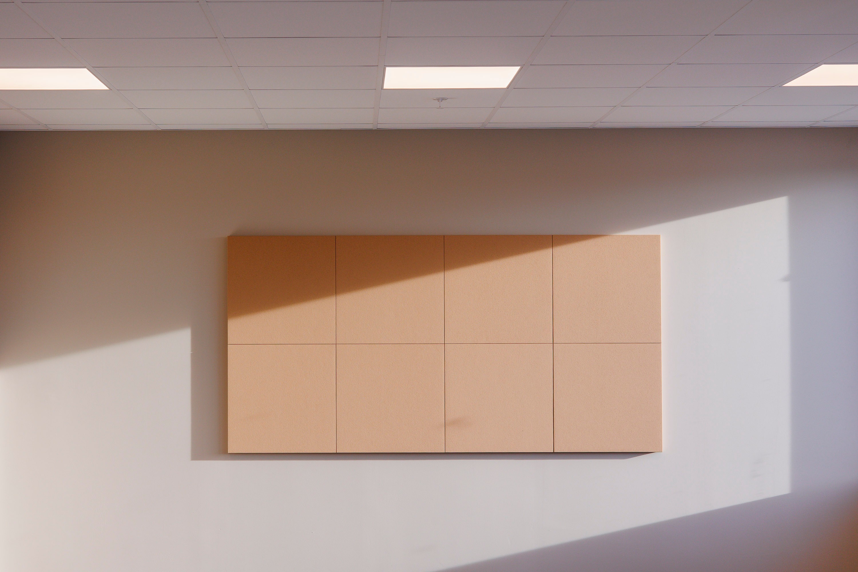 Beige akustiske veggpaneler med skyggemønstre under et hvitt tak i et moderne rom.