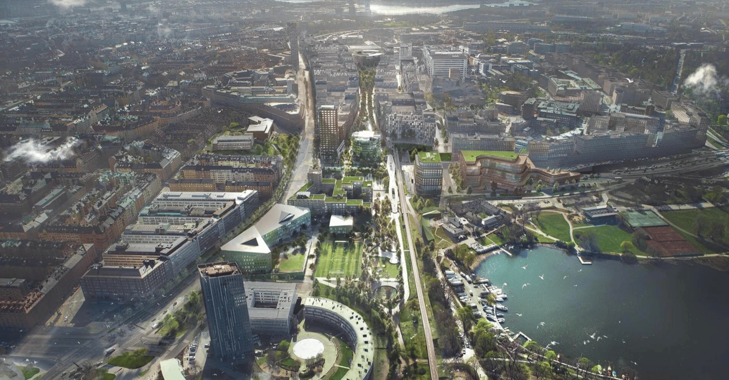 Flygfoto av ett modernt stadsområde med grönområden, byggnader och vattenfront.