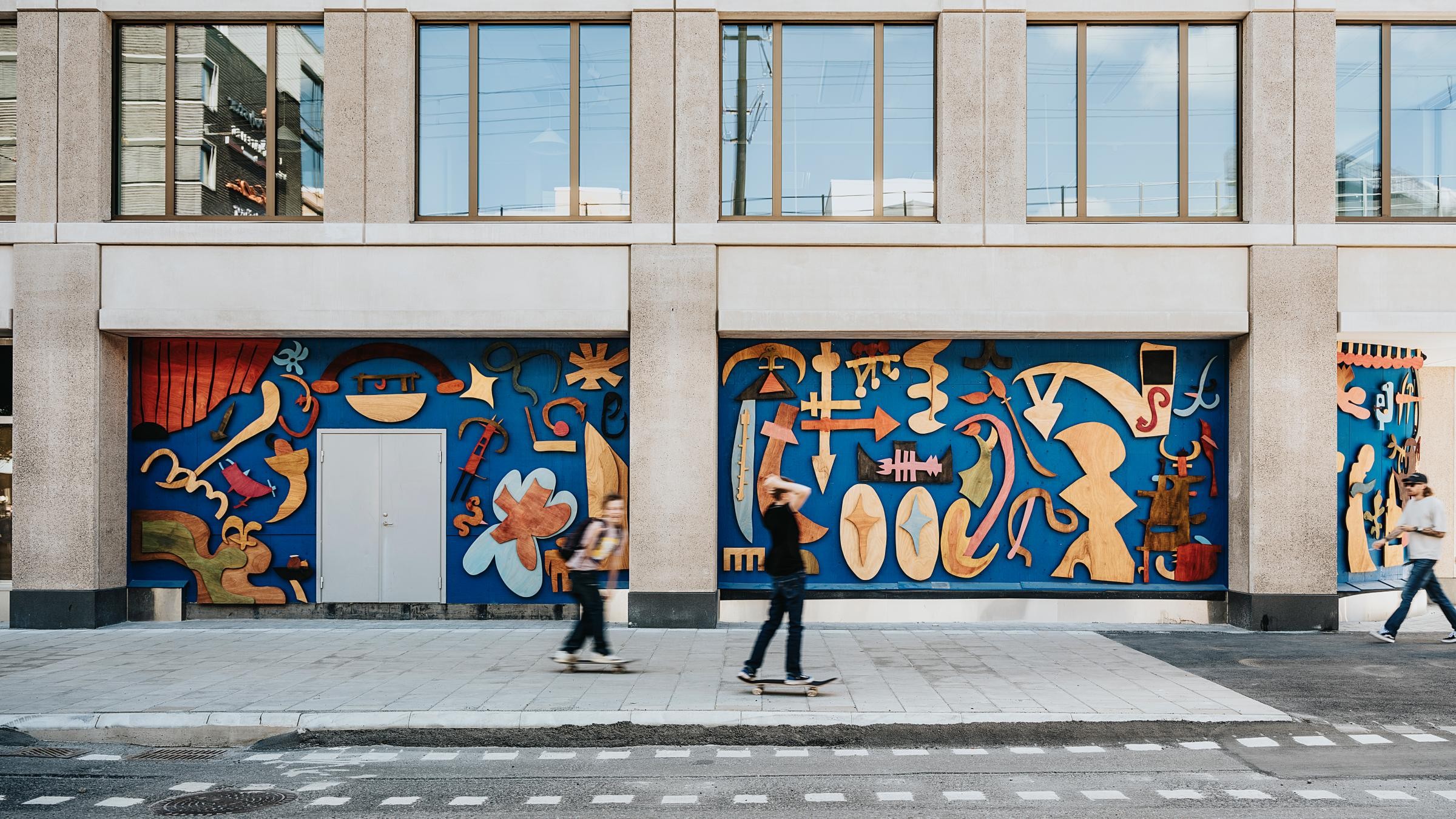 Färgglad urban mural med skateboardåkare på stadsgata Färgglad abstrakt muralmålning på stadens byggnadsfasad med skateboardåkare som passerar förbi.
