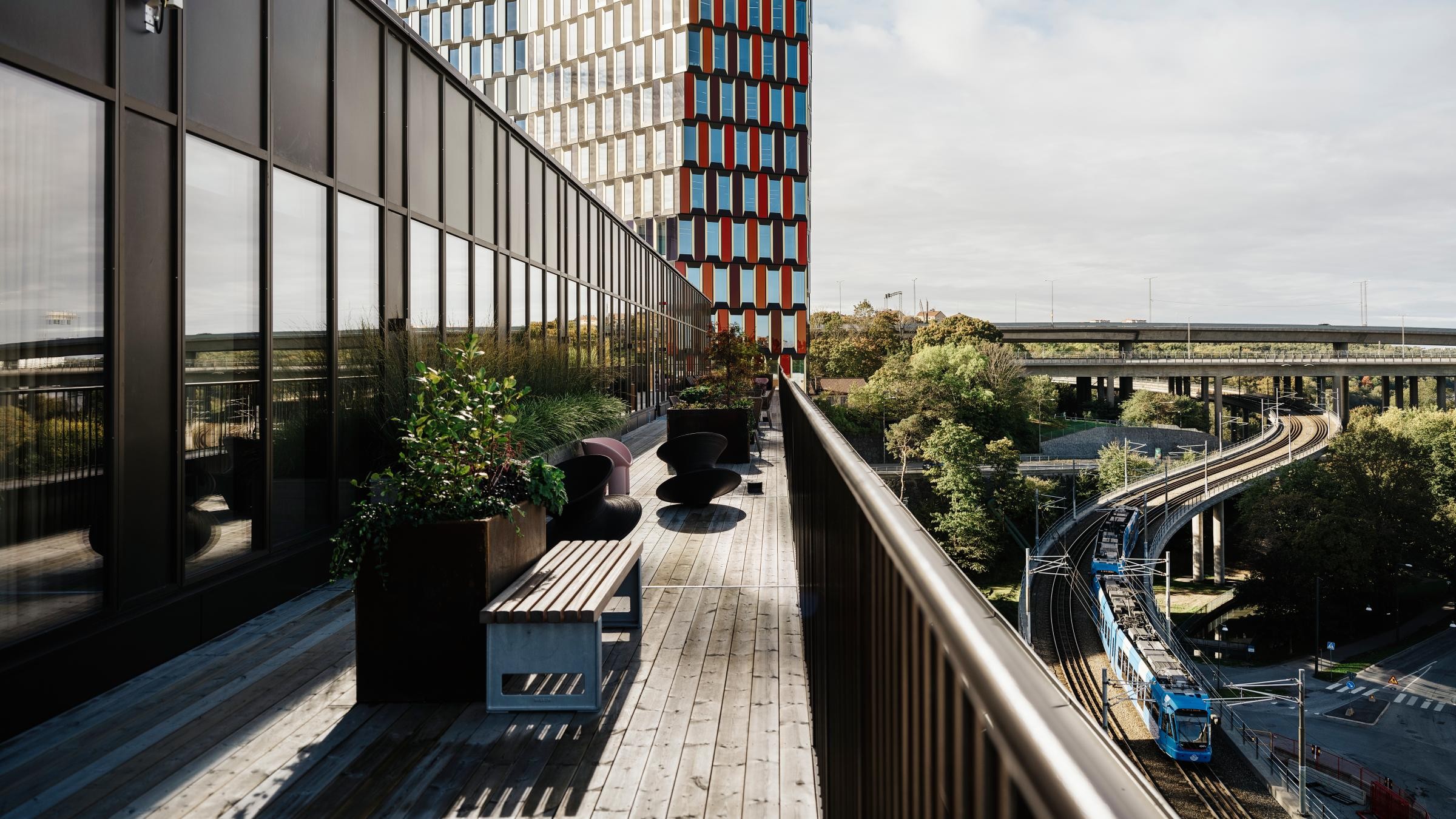 Modern takterrass med utsikt över en livlig stadsbild med frodig grönska och urban järnvägstransit.