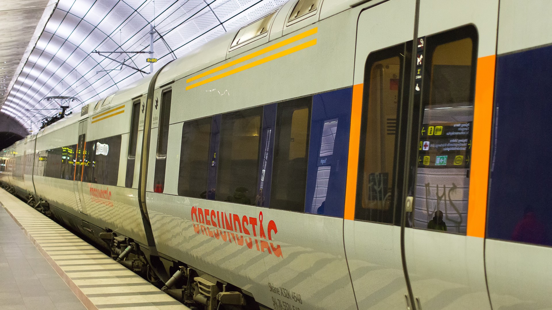 Modernt Öresundståg vid en väl upplyst stationsplattform under ett valvformat tak.