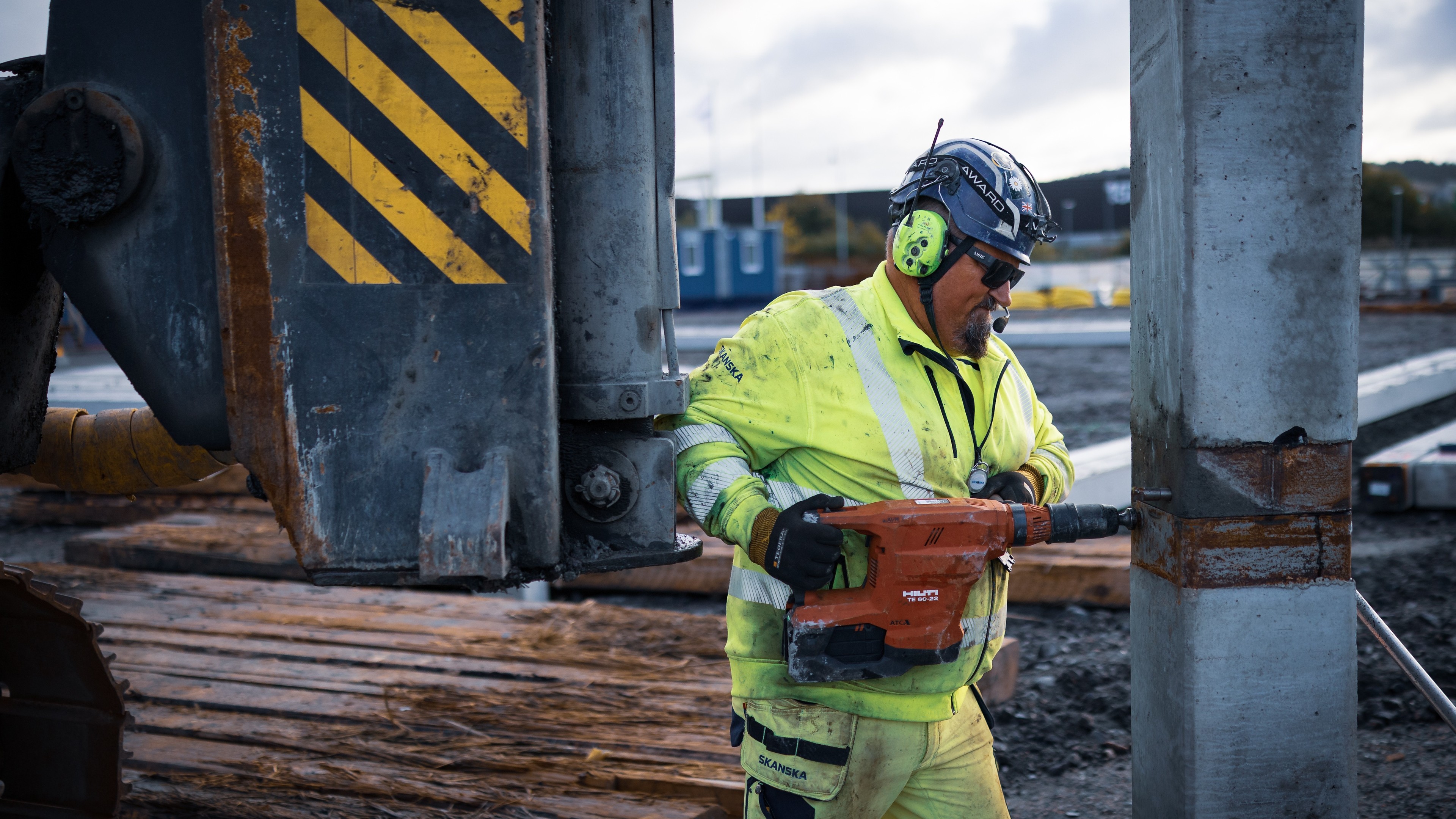 Byggnadsarbetare använder en slagborr på en betongpelare på en byggarbetsplats.