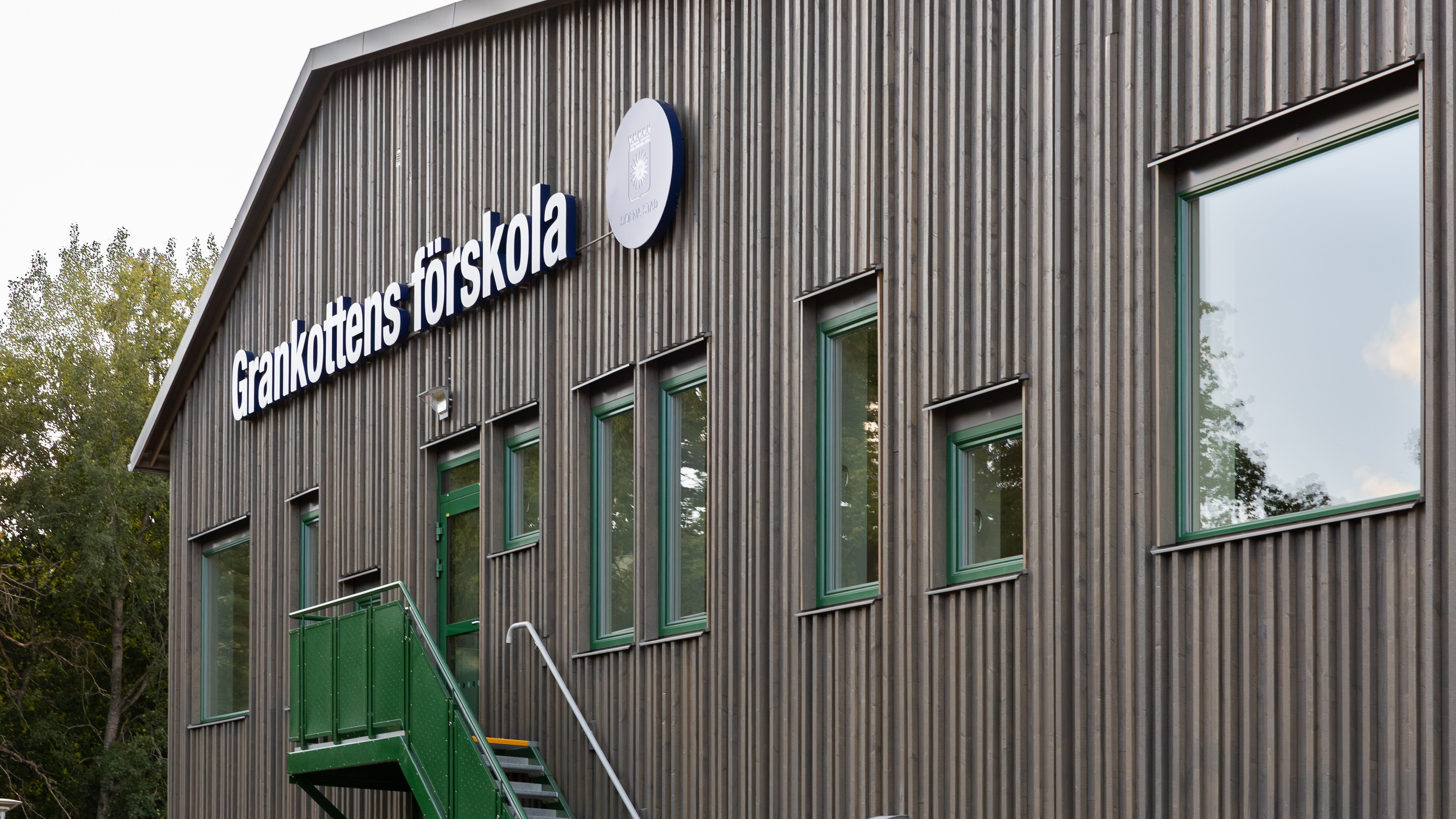 Exteriörvy av Grankottens förskola, en modern träförskolebyggnad med gröna fönster.